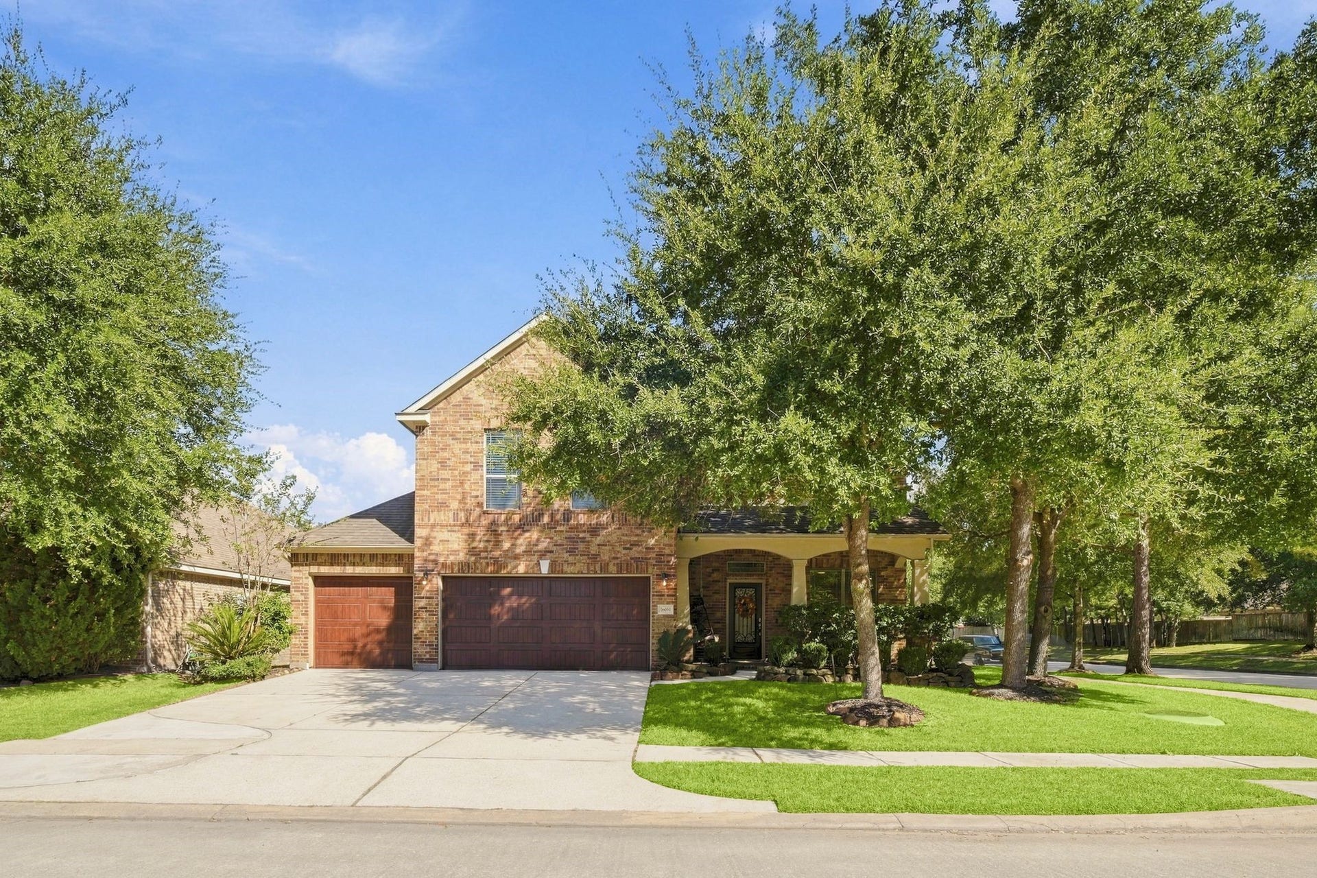 26037 Kings Mill Crest Drive, Kingwood, TX 77339 Charming brick home with a spacious three-car garage, nestled among mature trees and complemented by a well-manicured lawn.
