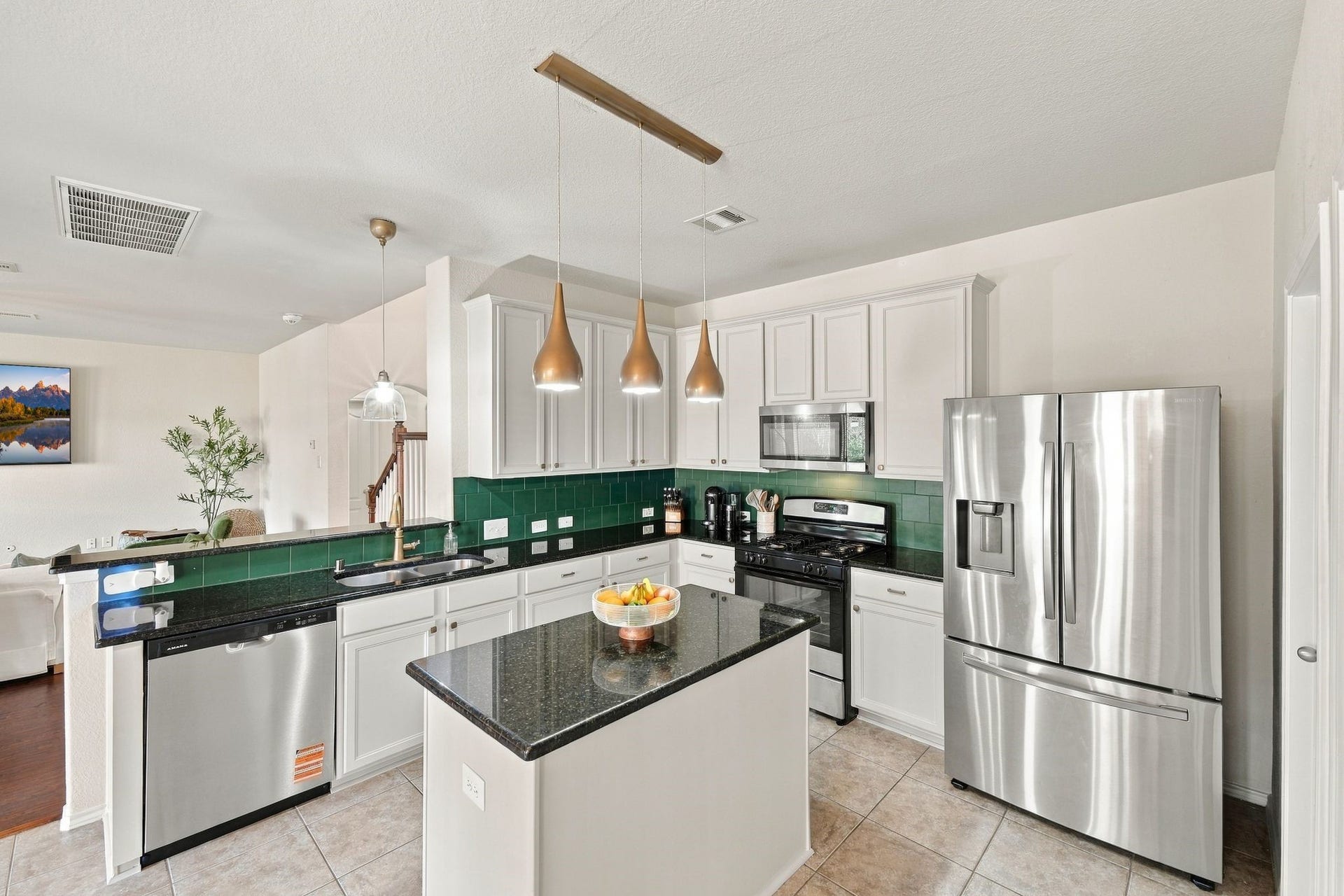 26037 Kings Mill Crest Drive, Kingwood, TX 77339 Modern kitchen with sleek stainless steel appliances, a central island with dark granite countertops, and stylish pendant lighting. The bright space features white cabinetry and a deep green tile backsplash, adding a touch of elegance.