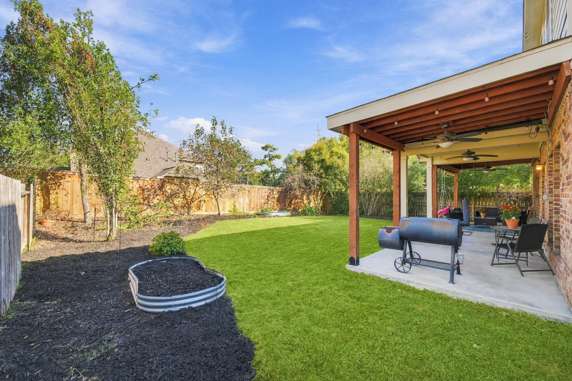 26037 Kings Mill Crest Drive, Kingwood, TX 77339 Spacious backyard featuring a covered patio with ceiling fans, perfect for outdoor gatherings, and a well-maintained lawn with surrounding greenery.