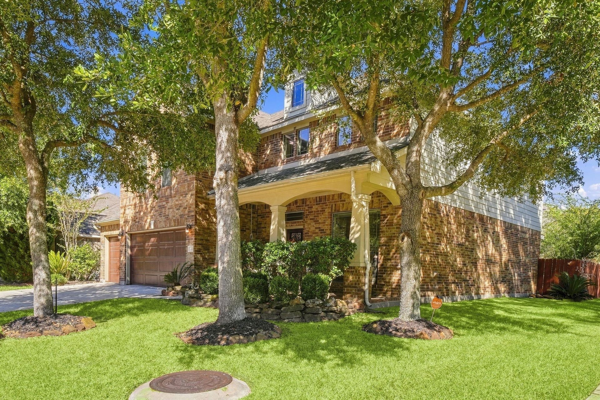 26037 Kings Mill Crest Drive, Kingwood, TX 77339 Charming two-story brick home with a welcoming front porch, surrounded by mature trees and lush landscaping, offering ample shade and curb appeal.