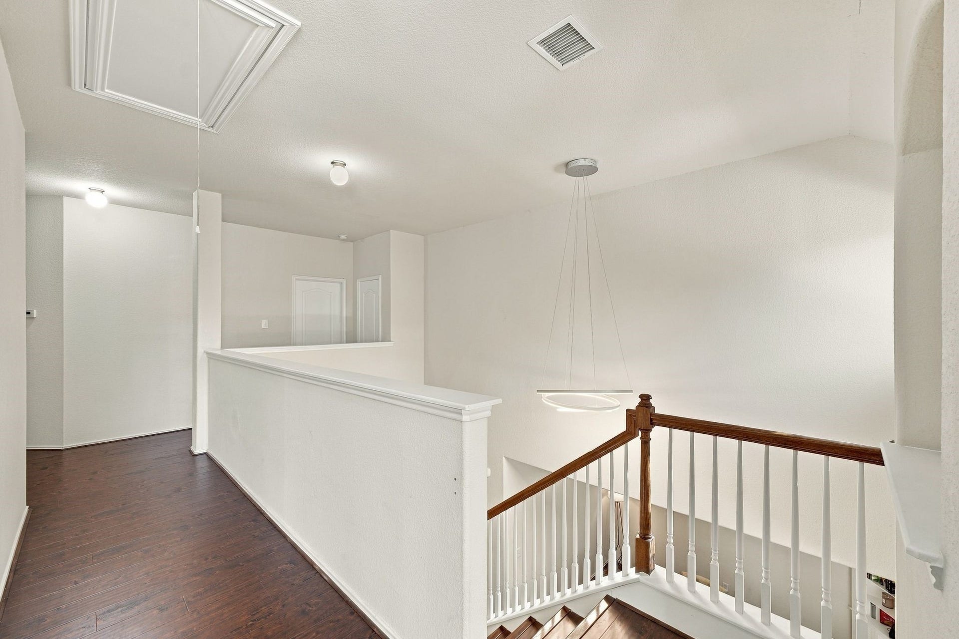 26037 Kings Mill Crest Drive, Kingwood, TX 77339 Bright and airy upstairs landing with elegant wood flooring and a modern light fixture, offering access to multiple rooms.