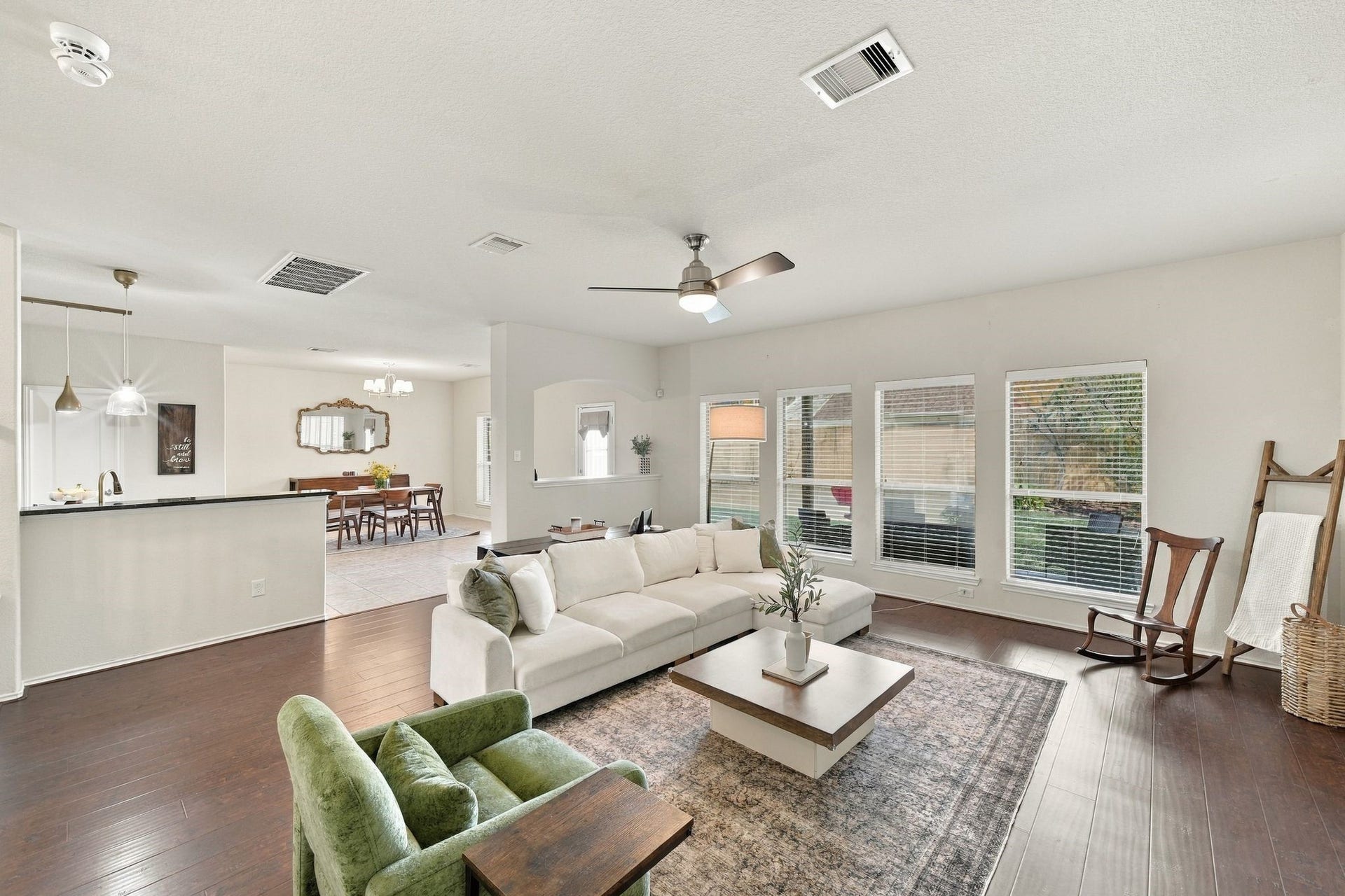 26037 Kings Mill Crest Drive, Kingwood, TX 77339 Spacious and bright open-concept living area with large windows, hardwood floors, and modern ceiling fan, seamlessly flowing into a dining space and kitchen with stylish pendant lighting.