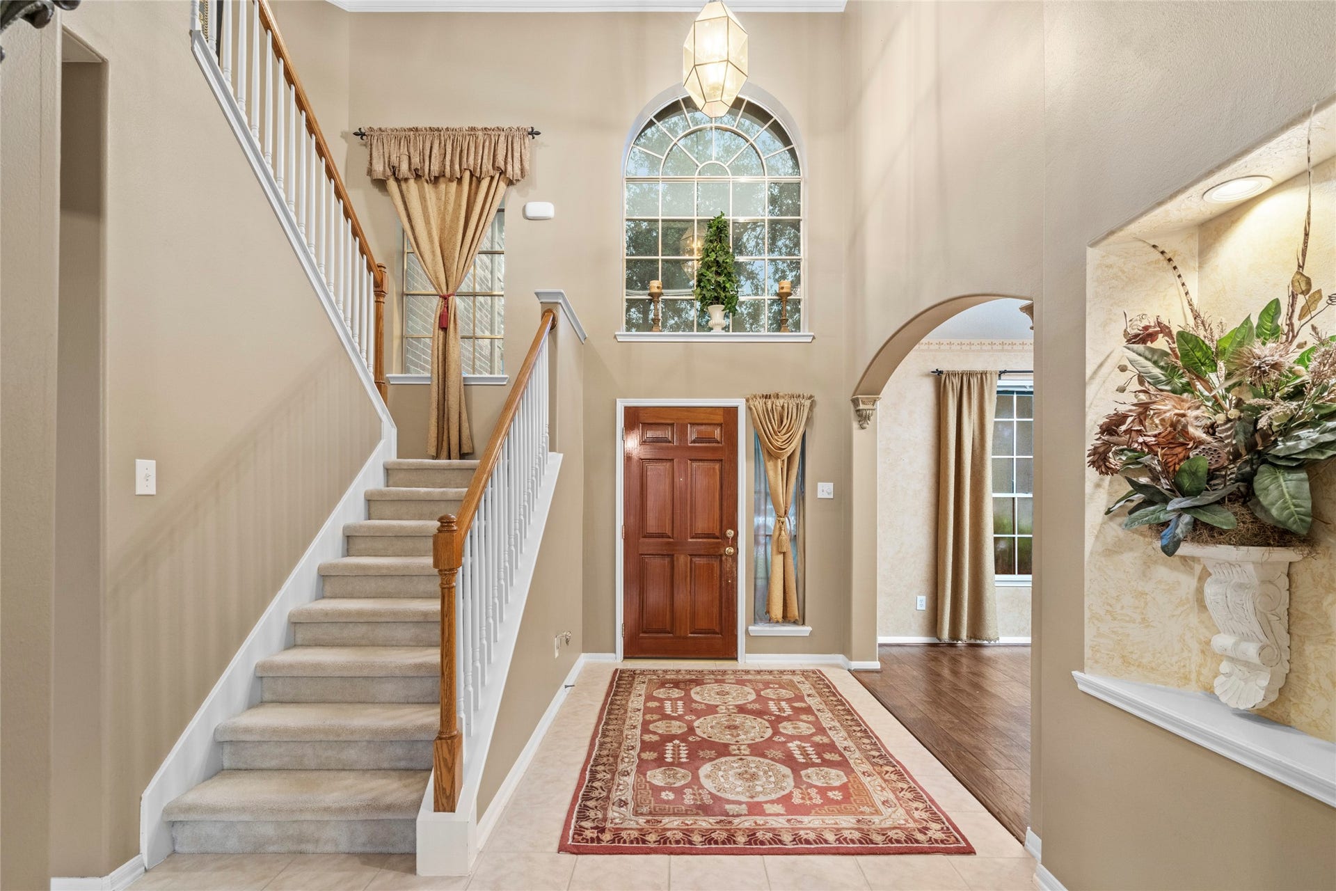 Grand entry foyer with soaring ceilings, an impressive staircase, arched window, and warm architectural details. The open entry creates an inviting first impression and gives the home a sense of space that continues throughout the main level.