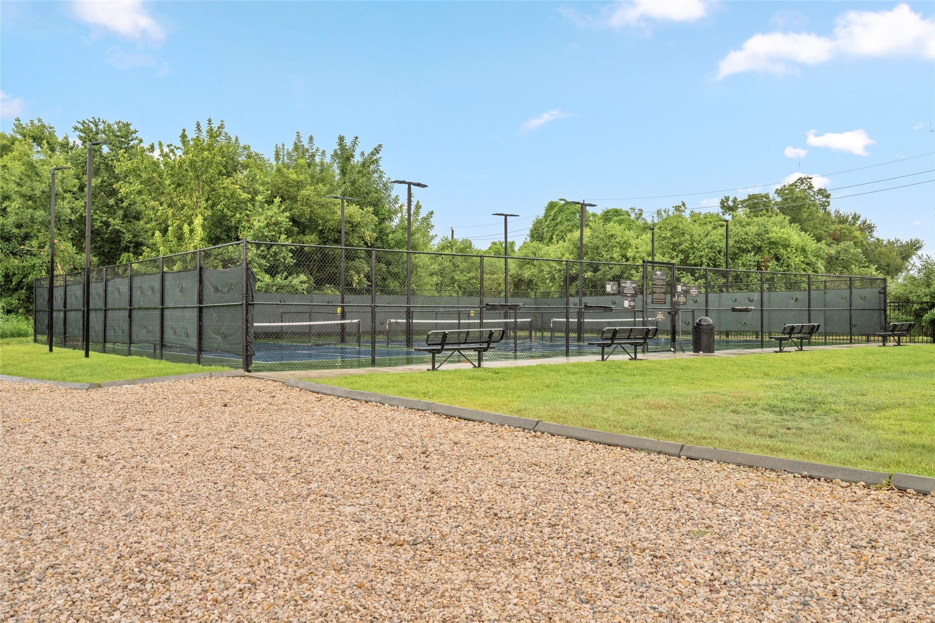 Neighborhood pickle ball court surrounded by mature greenery with seating for spectators. The amenity adds another layer of recreational convenience and reinforces the lifestyle appeal of the surrounding community.