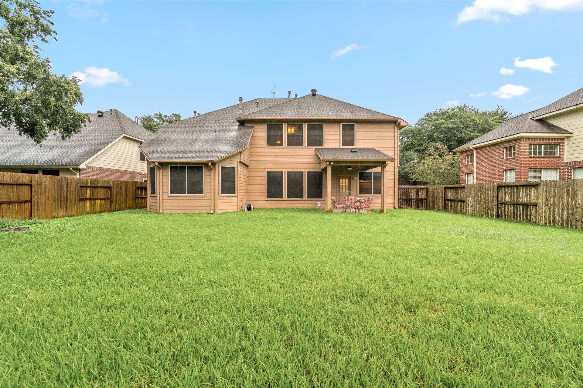 Expansive backyard with a broad lawn and attractive rear view of the two-story home. The combination of outdoor space, mature surroundings, and covered patio creates room for recreation, pets, gardening, and future outdoor living.