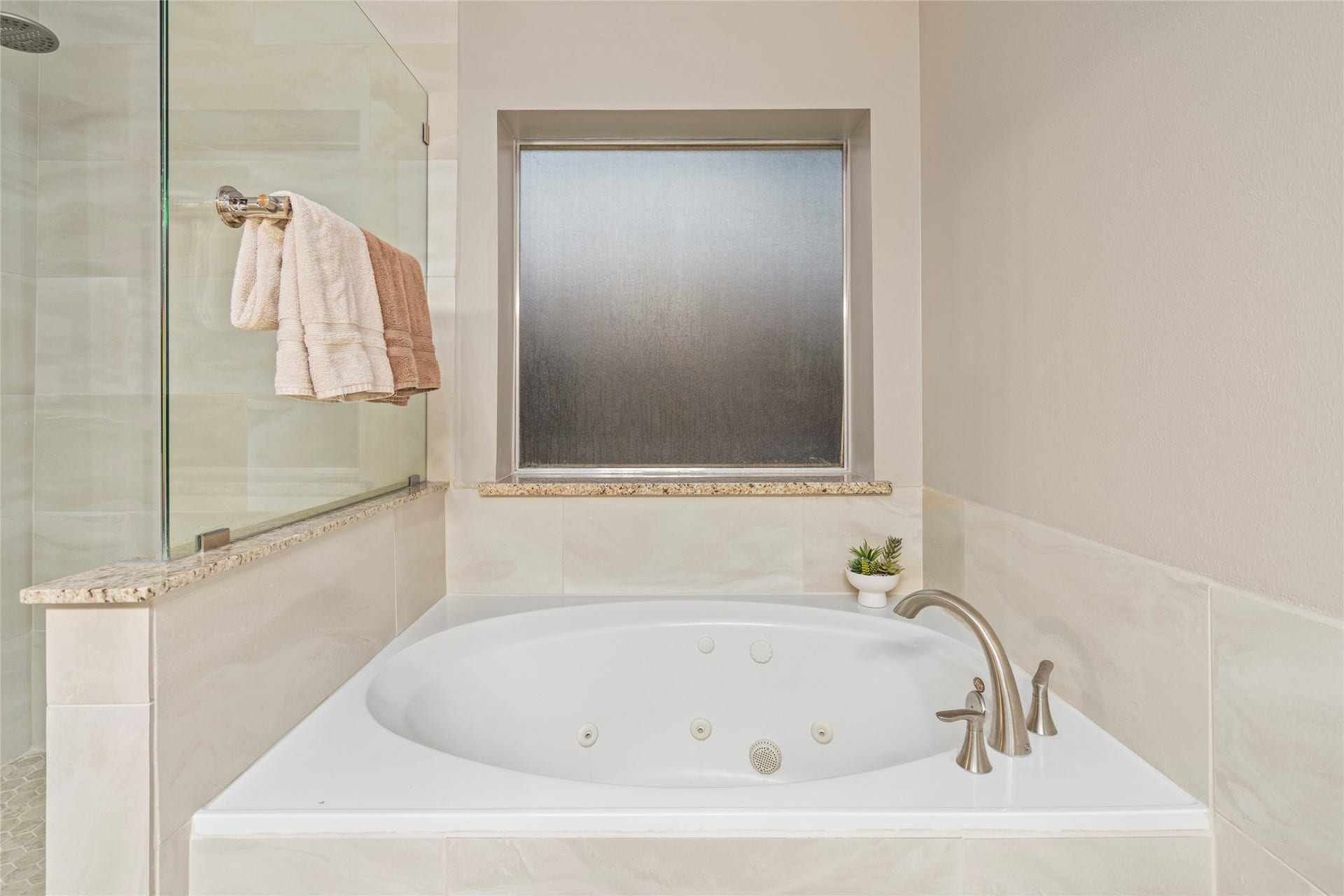 A closer view emphasizes the spacious tub, separate glass-enclosed shower, privacy-focused window, and generous overall layout. The primary bathroom was updated, including the shower area, adding to the home's appeal for buyers seeking a comfortable owner's retreat.