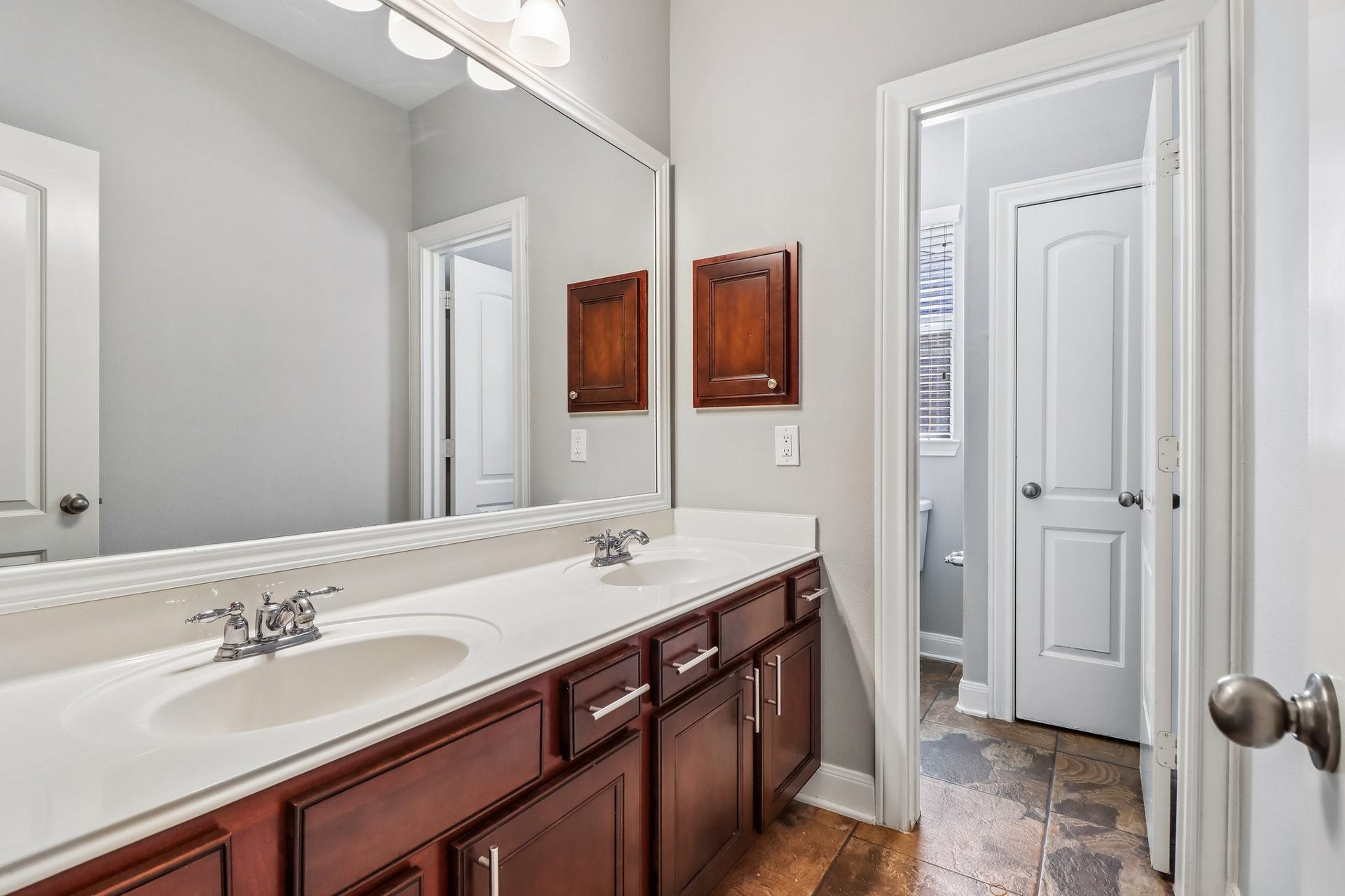 22715 Wilbur Lane, Tomball, TX 77375 Elegant bathroom featuring a double vanity with rich wood cabinetry and sleek fixtures, leading to a separate toilet area with natural light.