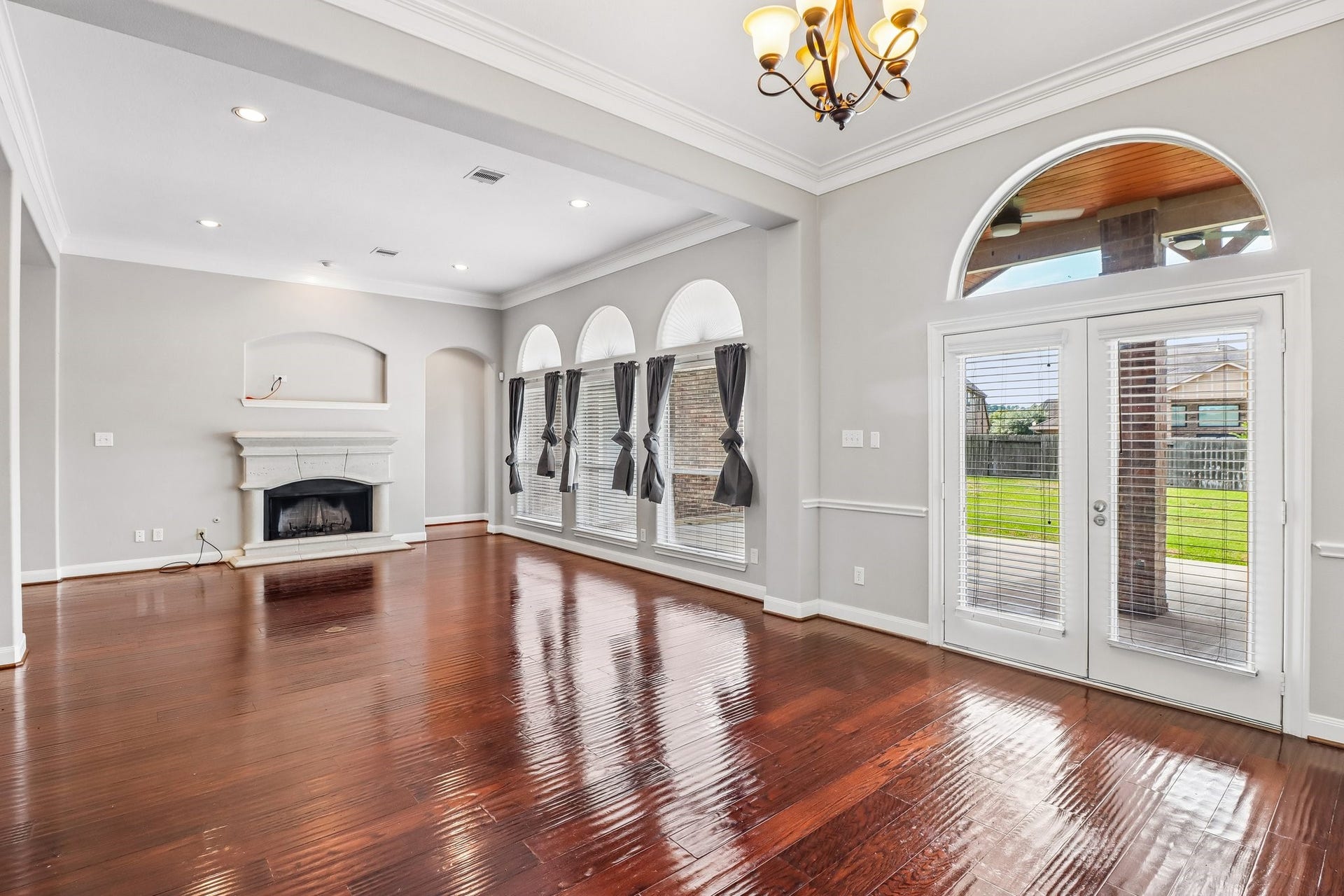 22715 Wilbur Lane, Tomball, TX 77375 Spacious living area with elegant hardwood floors, a cozy fireplace, and abundant natural light from arched windows and French doors leading to a lush backyard.