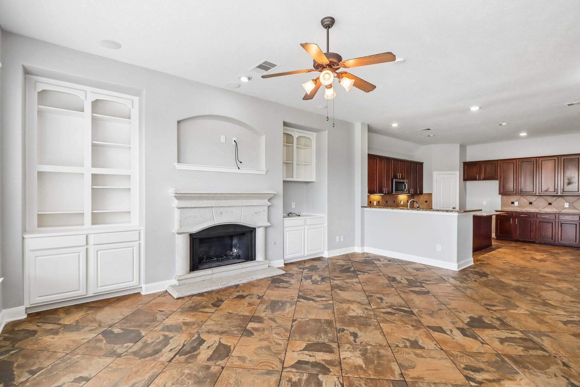 22715 Wilbur Lane, Tomball, TX 77375 Spacious living area featuring elegant tile flooring, a cozy fireplace with built-in shelving, and an open-concept kitchen with rich wood cabinetry and modern appliances.