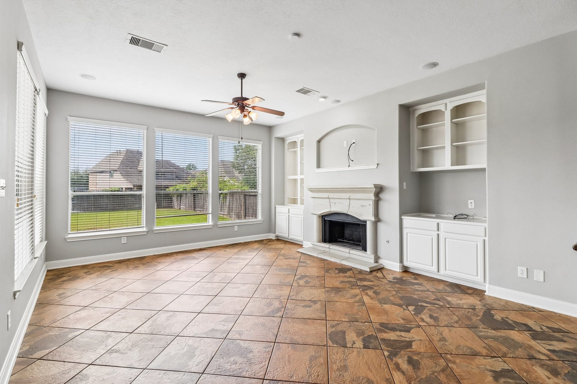 22715 Wilbur Lane, Tomball, TX 77375 Bright and spacious living area featuring large windows, a cozy fireplace, built-in shelving, and elegant tile flooring, offering a perfect blend of comfort and style.