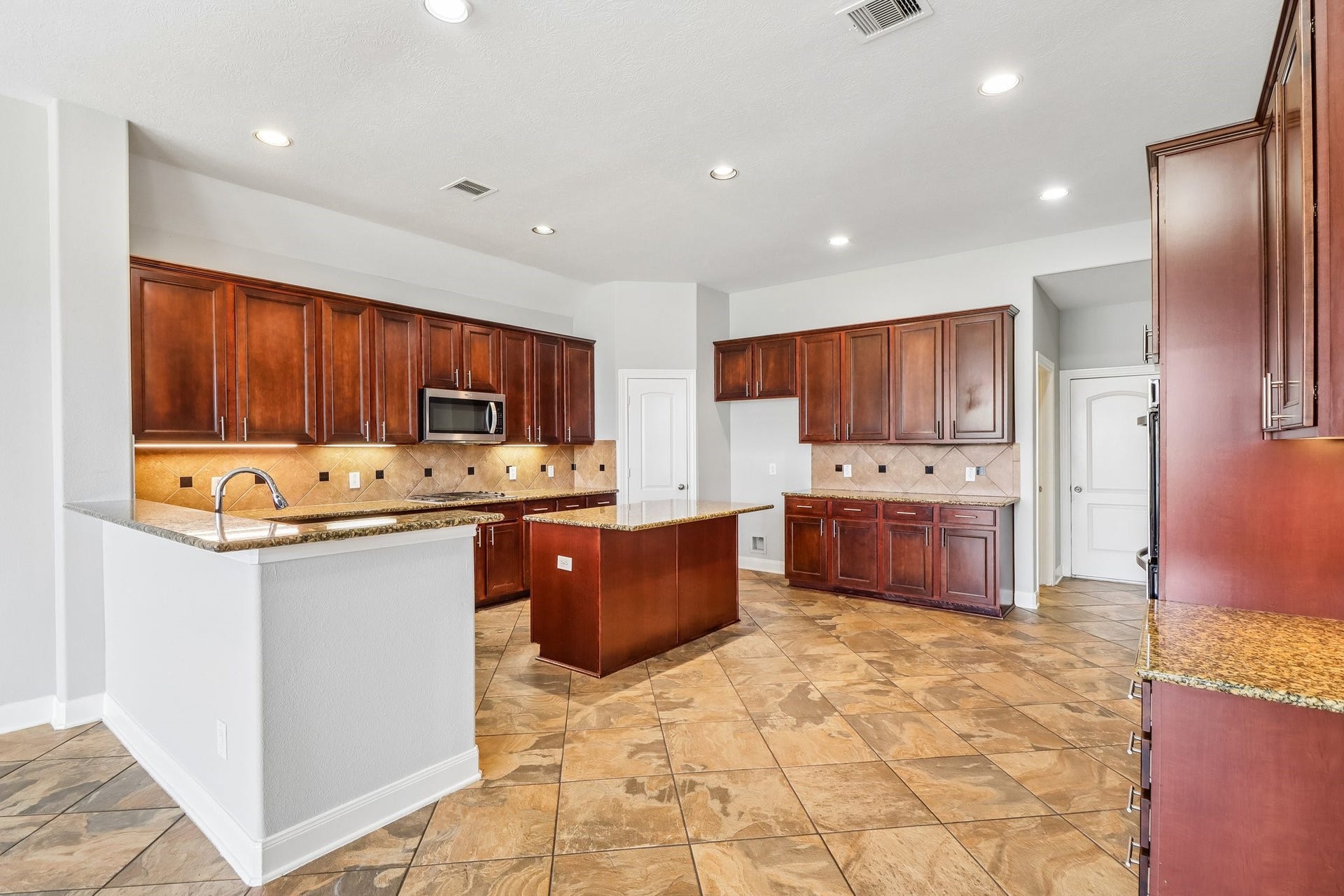 22715 Wilbur Lane, Tomball, TX 77375 Spacious kitchen with elegant dark wood cabinetry, granite countertops, and a central island, complemented by stylish tile flooring and modern stainless steel appliances.