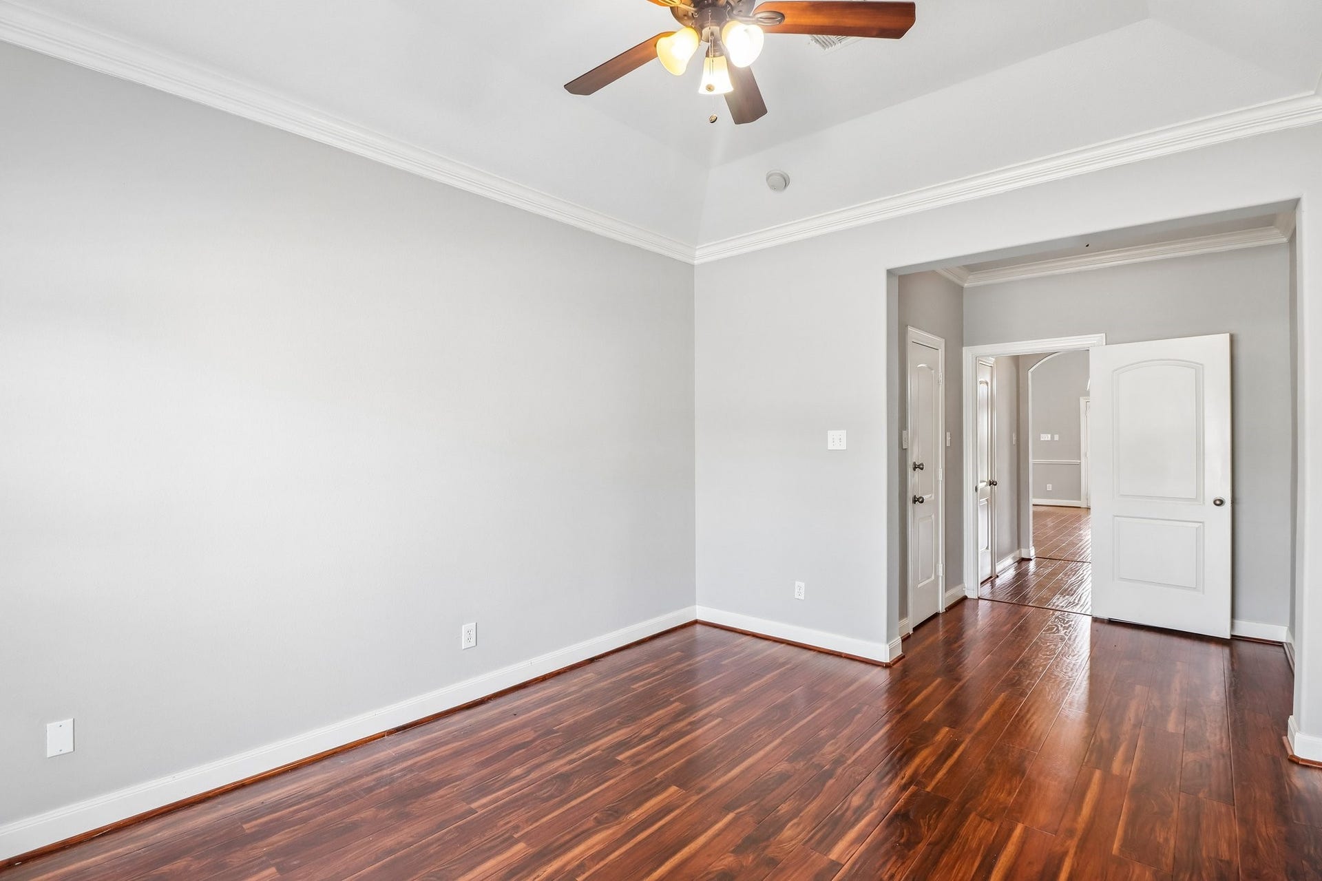 22715 Wilbur Lane, Tomball, TX 77375 Spacious room with elegant wood flooring, neutral walls, and a ceiling fan, leading to an adjoining area through a stylish doorway.