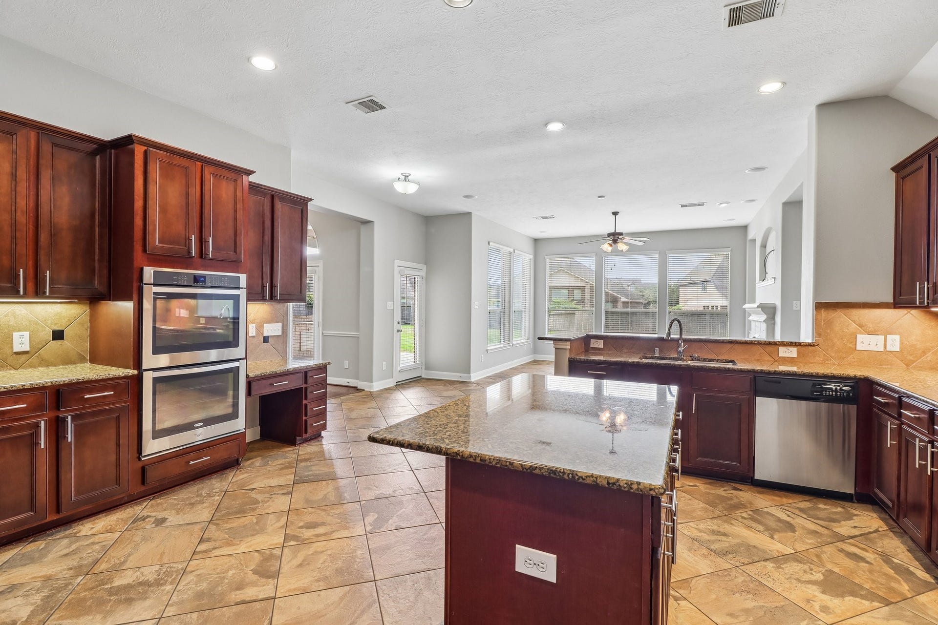 22715 Wilbur Lane, Tomball, TX 77375 Spacious kitchen with rich wood cabinetry, granite countertops, a large island, and stainless steel appliances. Abundant natural light streams through large windows, complementing the open layout and tiled floors.