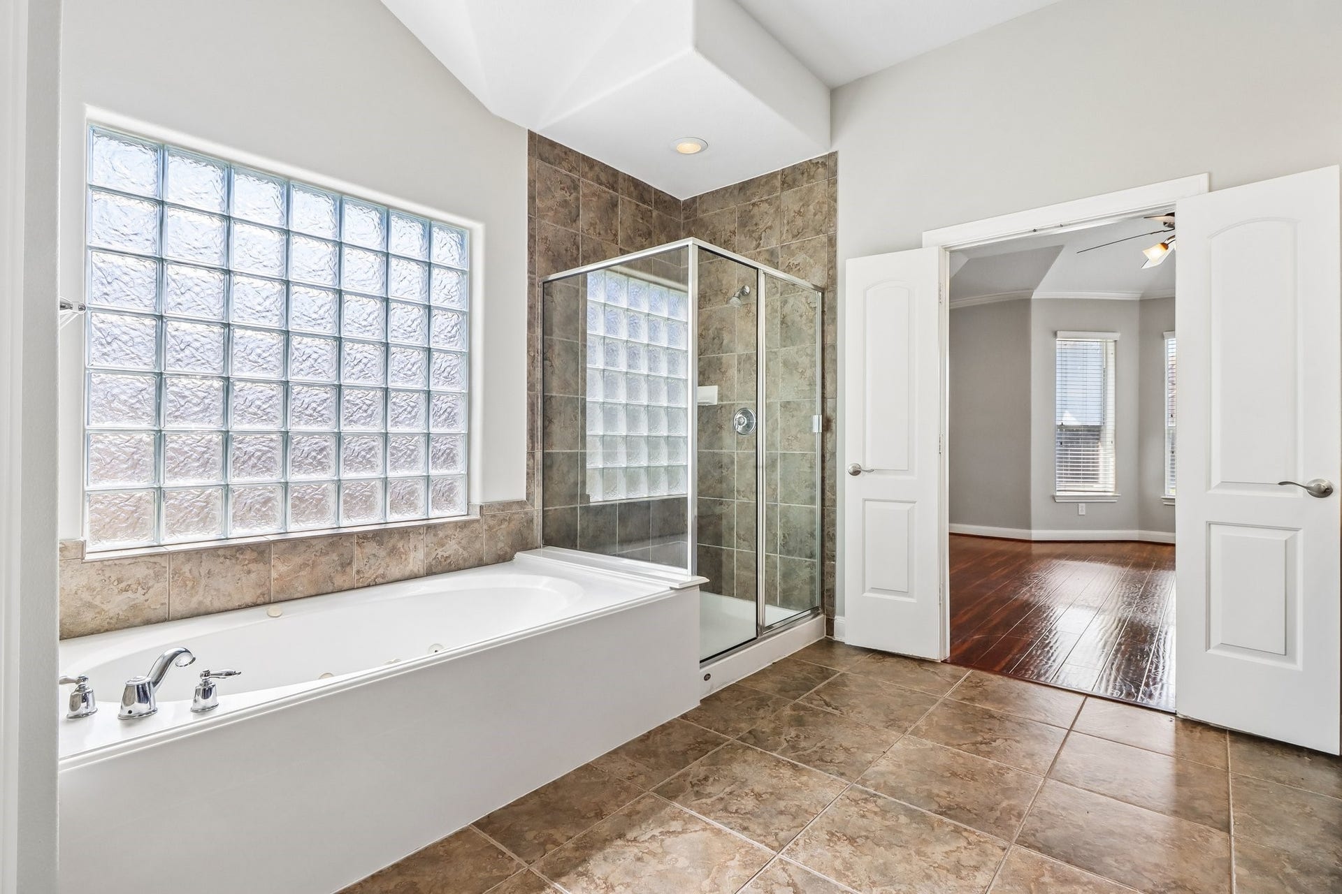 22715 Wilbur Lane, Tomball, TX 77375 Luxurious bathroom featuring a spacious soaking tub, glass-enclosed shower, and elegant tile flooring, seamlessly connected to an adjoining room with rich hardwood floors.