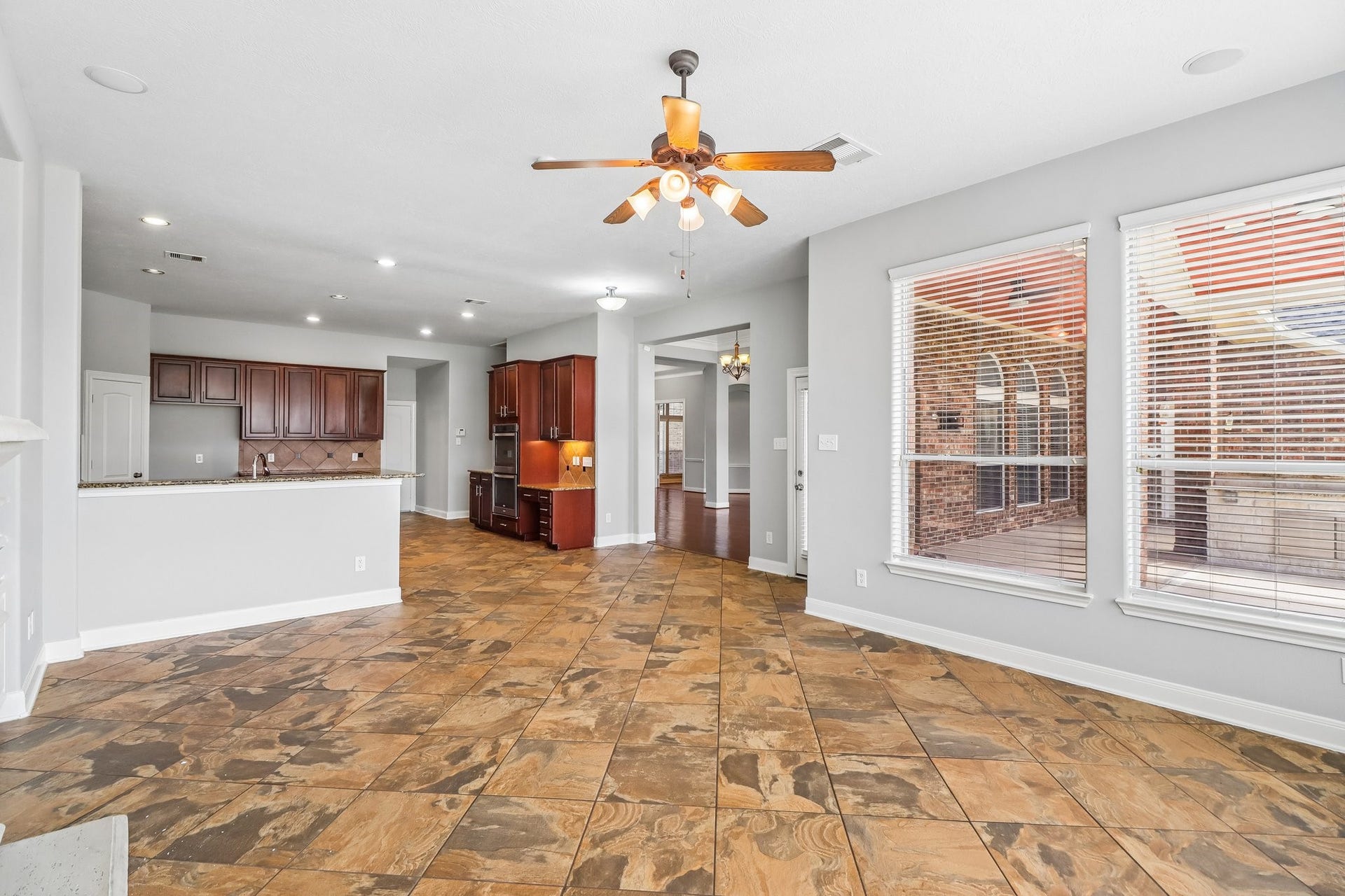 22715 Wilbur Lane, Tomball, TX 77375 Spacious open-concept living area with elegant tile flooring, large windows for natural light, and a ceiling fan. The kitchen features granite countertops and rich wood cabinetry, leading to a cozy corner workspace.