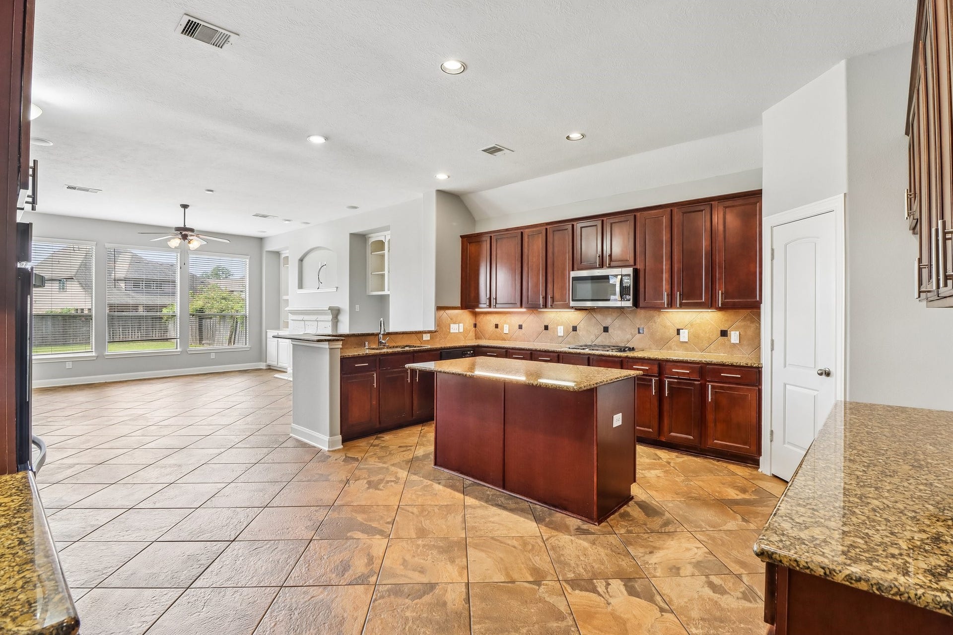 22715 Wilbur Lane, Tomball, TX 77375 Spacious open-concept kitchen and living area featuring sleek dark wood cabinetry, granite countertops, a central island, and large windows offering abundant natural light.