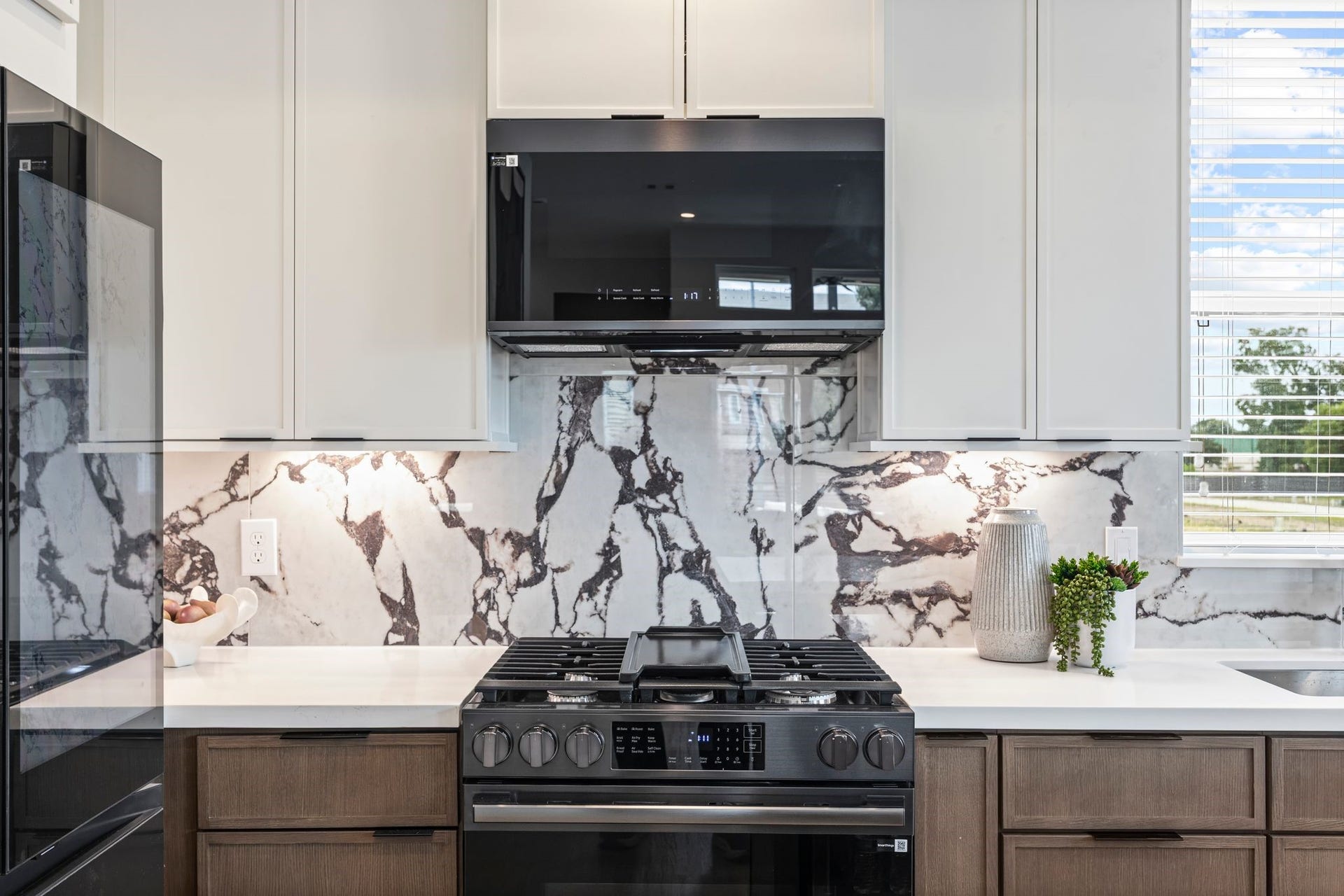 Sleek and modern kitchen featuring elegant marble-patterned backsplash, state-of-the-art appliances, and ample natural light for a sophisticated culinary experience. **Model Home of similar layout & finishes.**