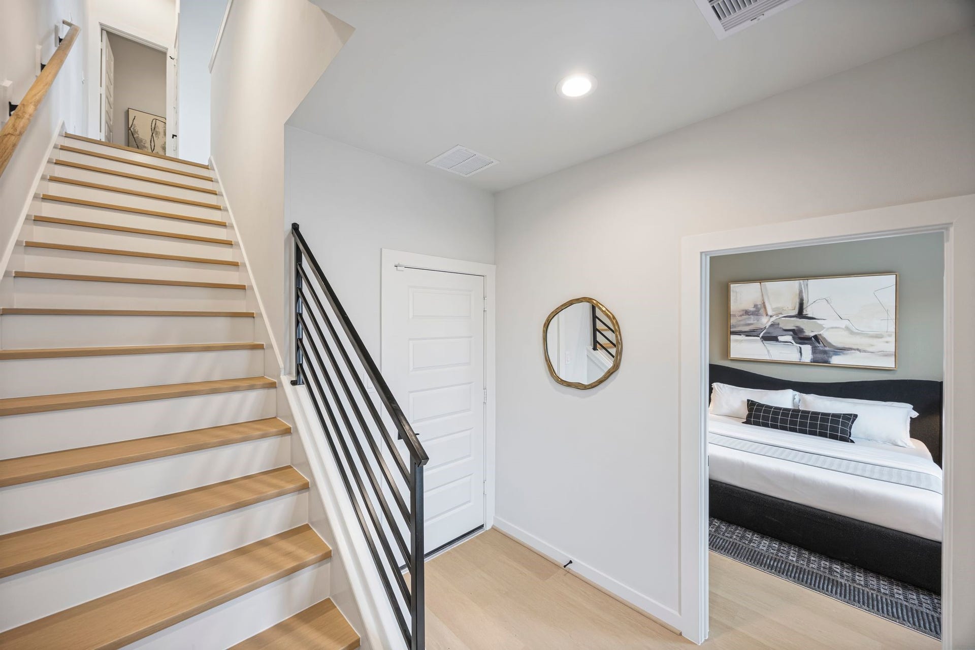 Step into a welcoming entrance featuring sleek wooden stairs, modern railings, and a glimpse of a cozy, art-adorned bedroom that promises comfort and style. **Model Home of similar layout & finishes.**