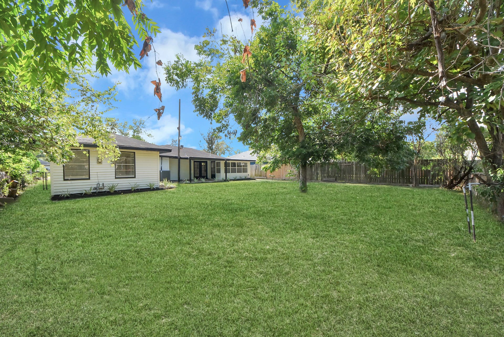 9610 Westview Drive, Houston, TX 77055 Expansive backyard with lush greenery and mature trees, perfect for outdoor activities and relaxation, complemented by a charming house and a private fence for added seclusion.