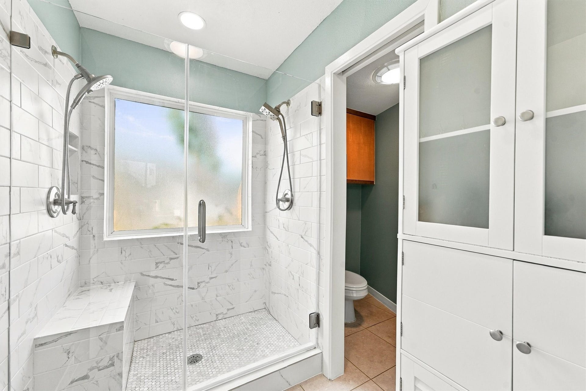 4207 Barataria Court, Galveston, TX 77554 A spacious glass-enclosed shower with dual showerheads and a built-in bench. Marble tile and soft natural light create a peaceful finish to your daily routine.