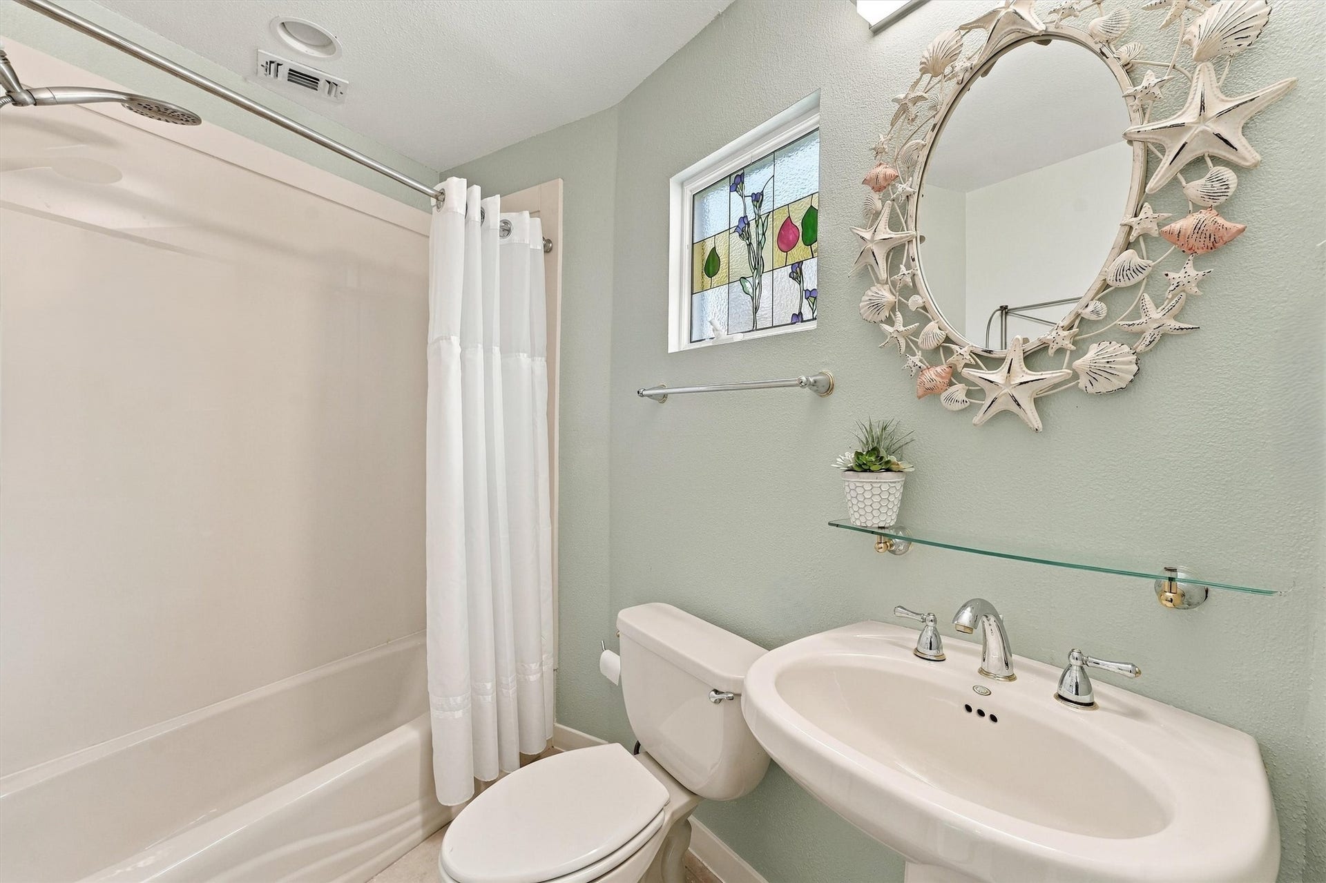 4207 Barataria Court, Galveston, TX 77554 A tub-and-shower combination, pedestal sink, decorative stained glass resting against the window, bring convenience and seaside personality together.