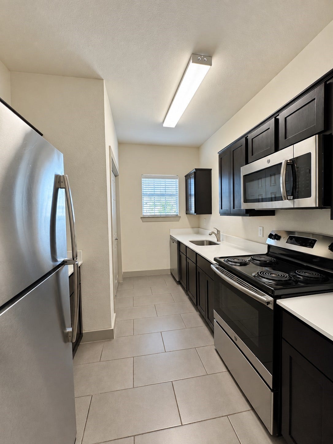 1660 Hawthorne Street, Houston, TX 77006 Representative unit kitchen. Galley-style kitchen in one of eight units, featuring dark cabinetry, tiled flooring, stainless steel appliances, and functional countertop space.