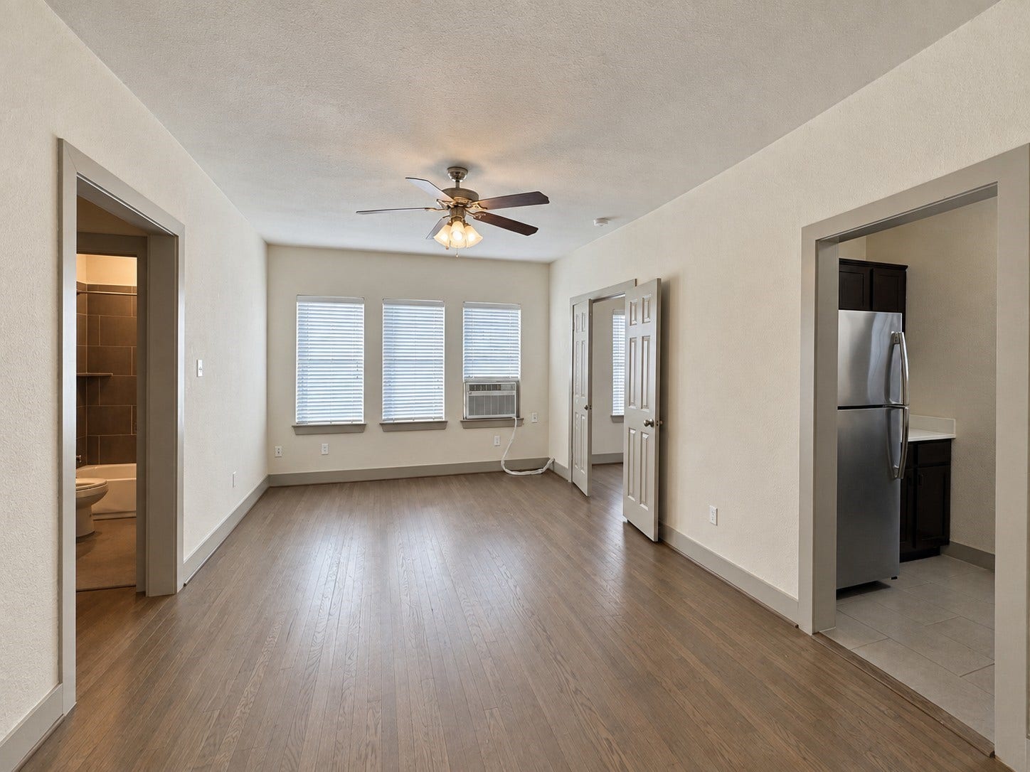 1660 Hawthorne Street, Houston, TX 77006 Representative unit living area. Interior view of one of the propertys eight residential units, featuring a bright living area with wood flooring, ceiling fan, multiple windows, and convenient access to the kitchen and adjoining rooms.