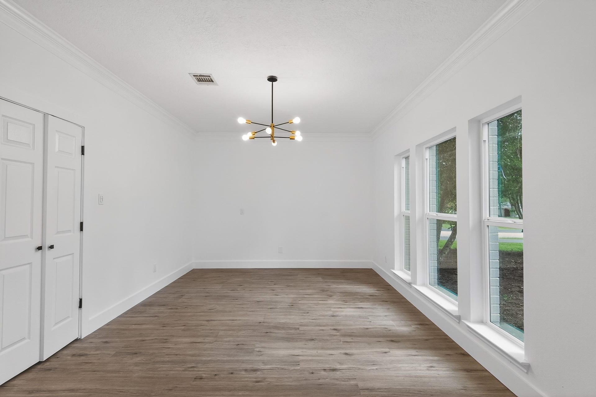 523 Rampart Lane, Conroe, TX 77302 Bright and inviting room with large windows, sleek luxury vinyl flooring, and a modern chandelier, perfect for a dining area or living space.