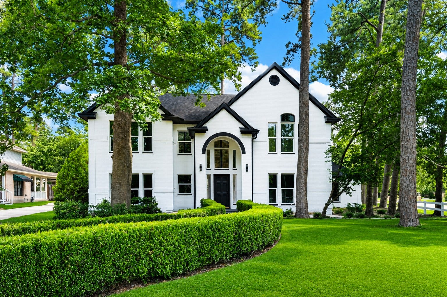 523 Rampart Lane, Conroe, TX 77302 Elegant two-story home with a striking white brick exterior, nestled among mature trees and lush greenery, featuring arched windows and a welcoming entryway. *Photo Digitally enhanced.