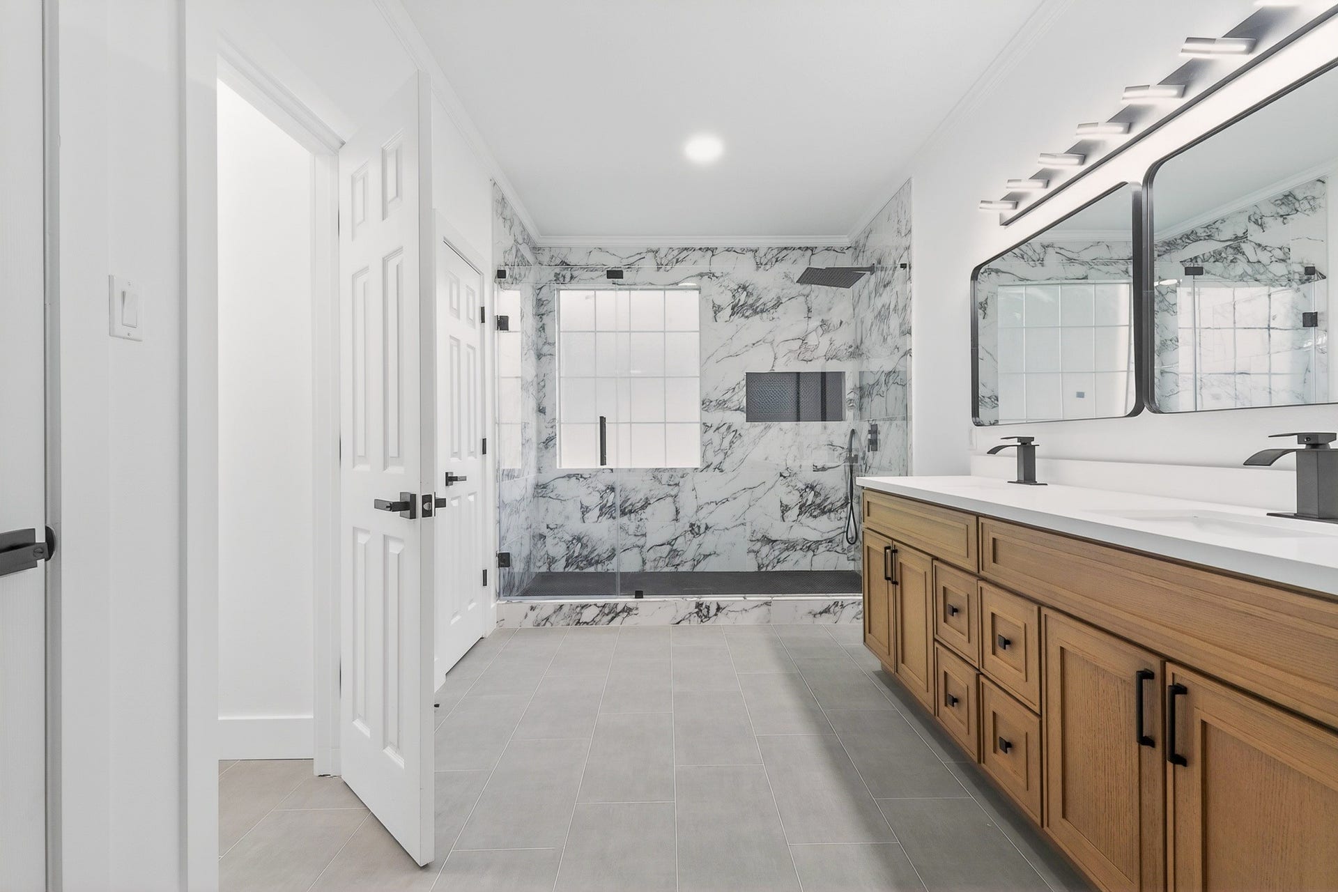 523 Rampart Lane, Conroe, TX 77302 Luxurious bathroom featuring a spacious walk-in shower with elegant marble walls, dual vanity with sleek black fixtures, and ample storage in warm wood cabinetry.