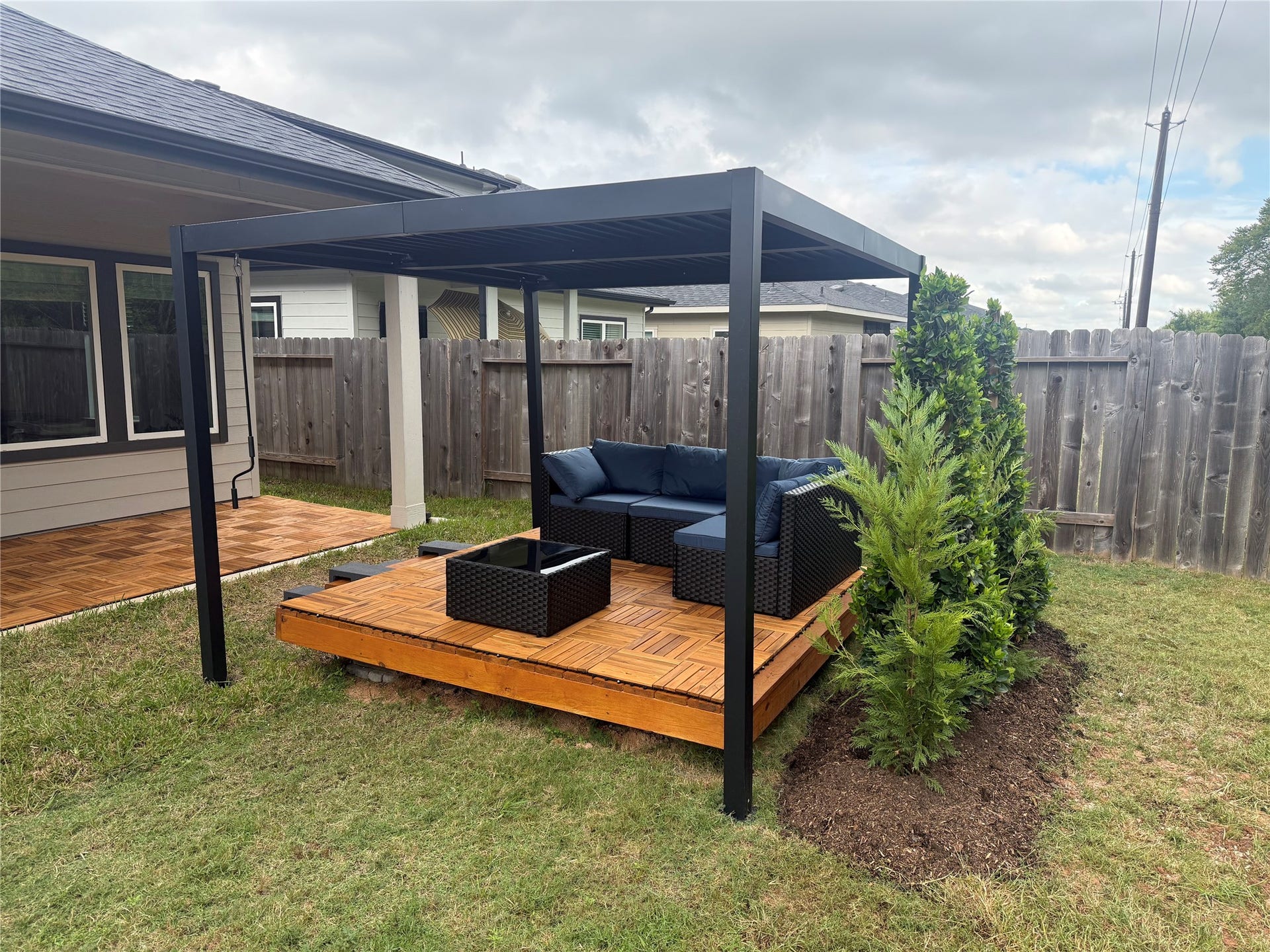 Newly added deck and modern pergola expand the homes outdoor living space, complemented by wood-look deck tiles on the covered patio and fresh backyard landscaping.