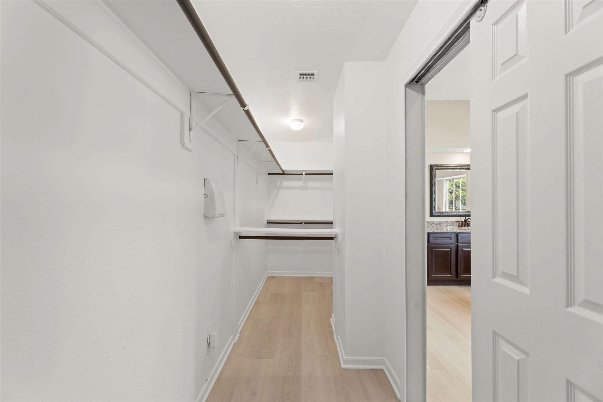 Ample hanging space in the walk-in closet. It opens to a room with dark wood cabinetry and a window.
