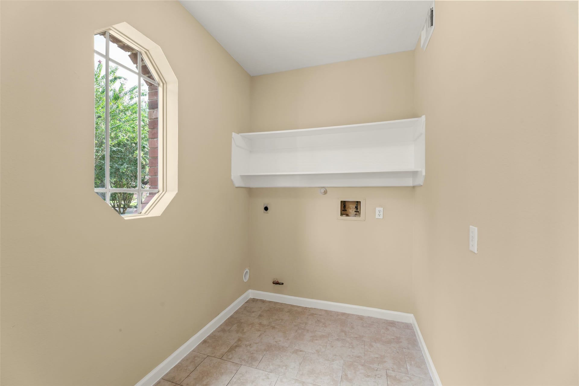 Laundry room with neutral walls, a tile floor, a large window for natural light, and a built-in shelf, making it ideal for a laundry or utility space.