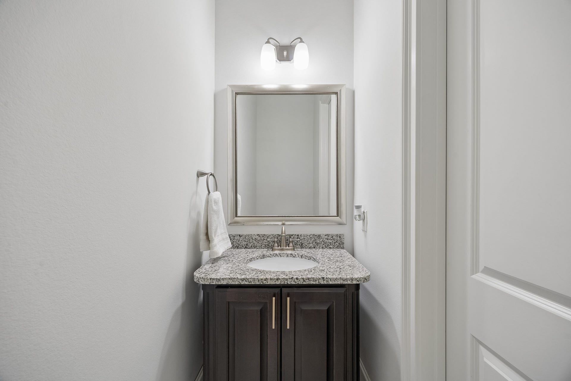 5018 Southampton Road, Missouri City, TX 77459 Elegant powder room featuring a sleek granite countertop and a stylish dark wood vanity, complemented by a framed mirror and modern lighting.