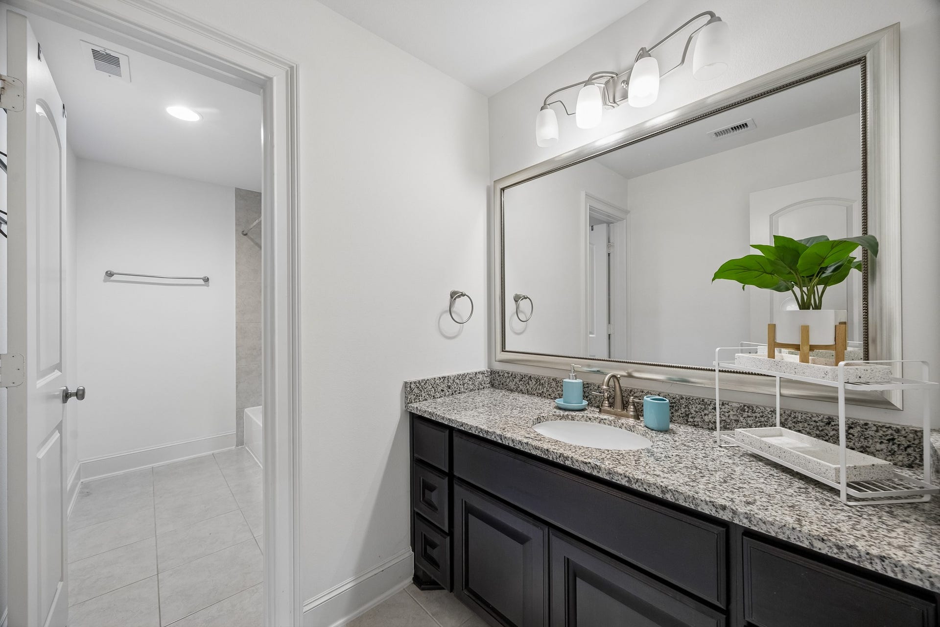 5018 Southampton Road, Missouri City, TX 77459 Spacious 2nd floor bathroom featuring a sleek granite countertop, elegant lighting, and ample storage with dark cabinetry, leading to a bright, tiled shower area.