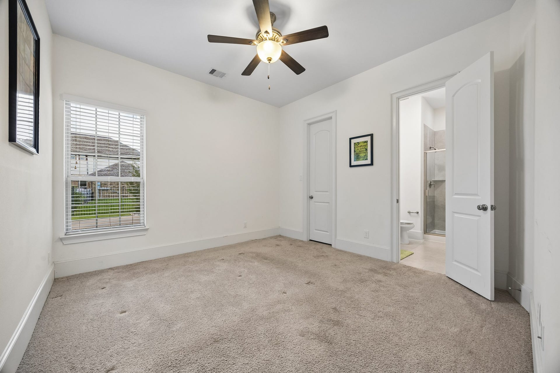 5018 Southampton Road, Missouri City, TX 77459 This inviting 1st floor secondary bedroom with plush carpet, ceiling fan, and abundant natural light from a large window, features an en-suite bathroom for added convenience.