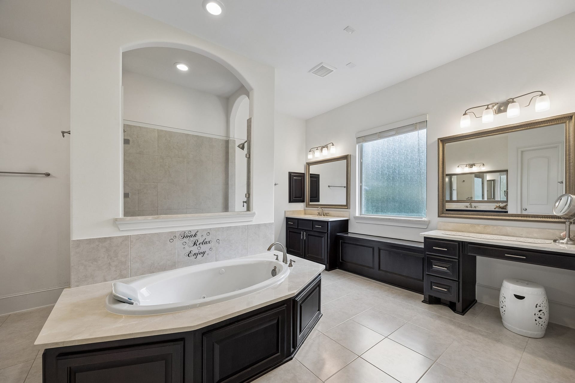 5018 Southampton Road, Missouri City, TX 77459 Luxurious bathroom featuring a spacious soaking tub, dual vanities with elegant dark cabinetry, and ample natural light from the large window.