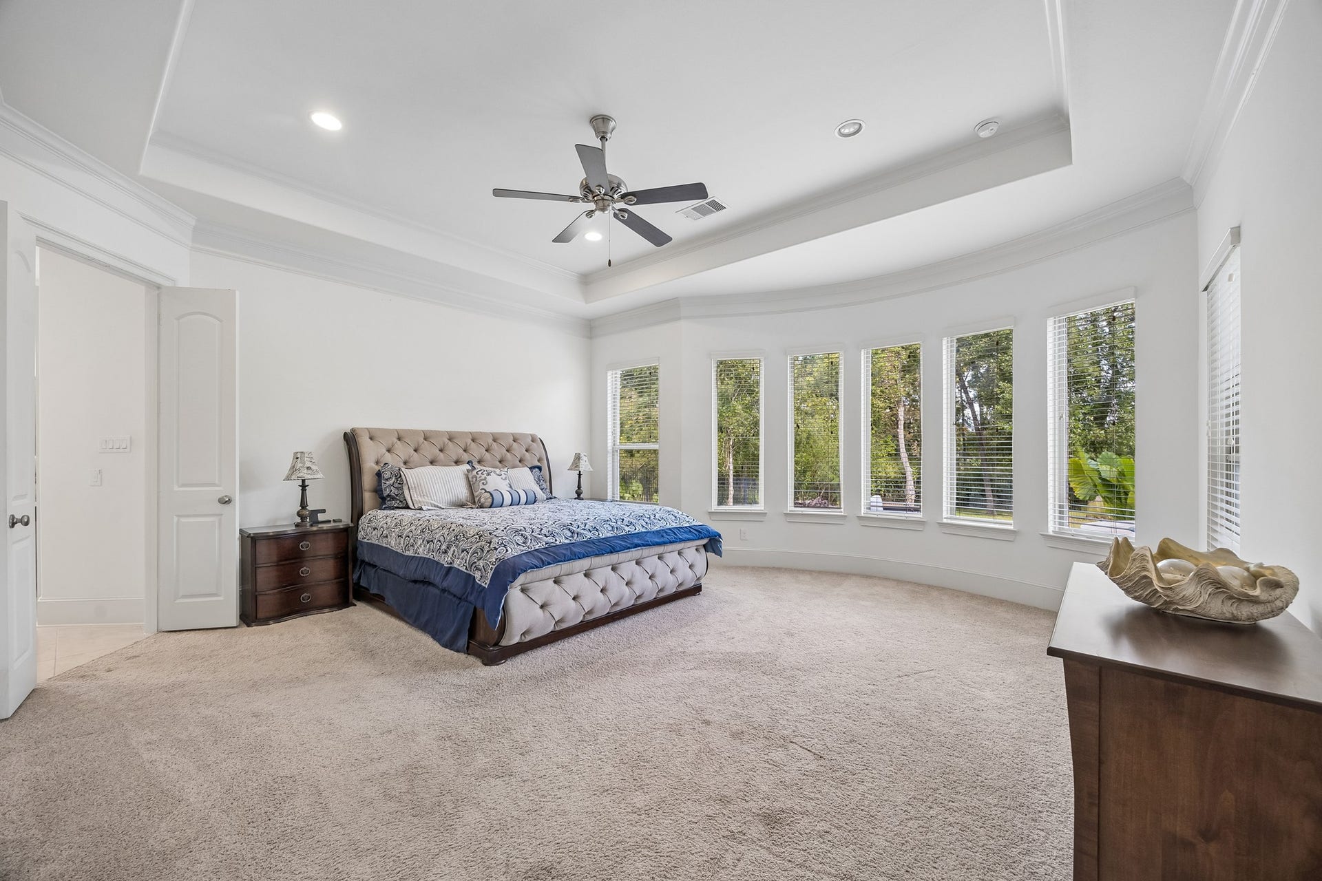 5018 Southampton Road, Missouri City, TX 77459 Primary bedroom with elegant tray ceiling, abundant natural light from a series of large windows that look out to the resort like pool, and plush carpeting, creating a cozy and inviting atmosphere.