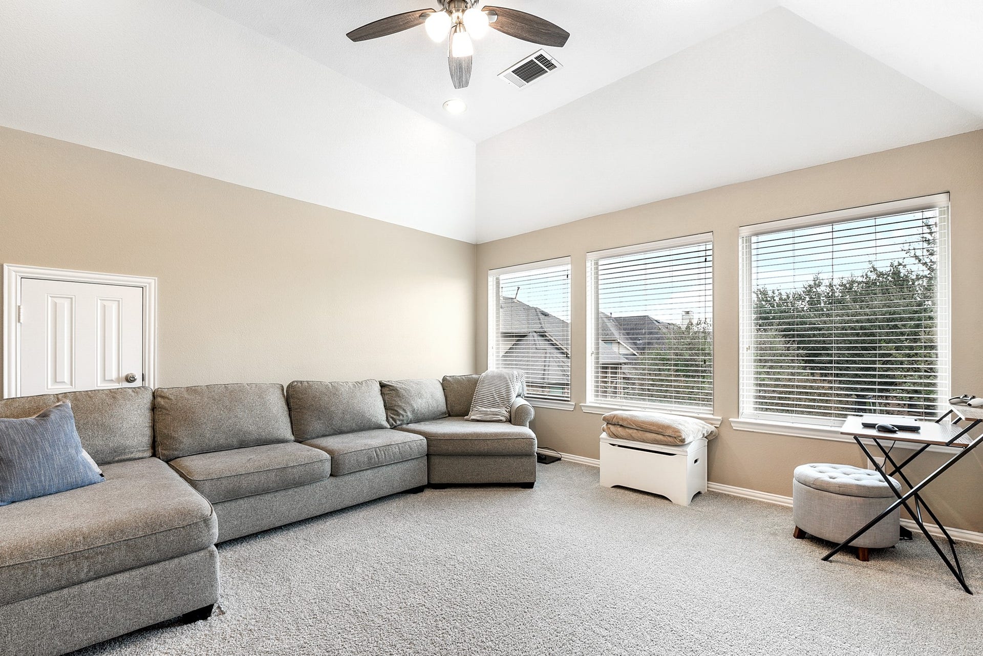 Another view of this spacious game room highlights its neutral paint scheme, ceiling fan, and large windows with a view of the backyard. The room also features high ceilings, adding to its open and airy feel.