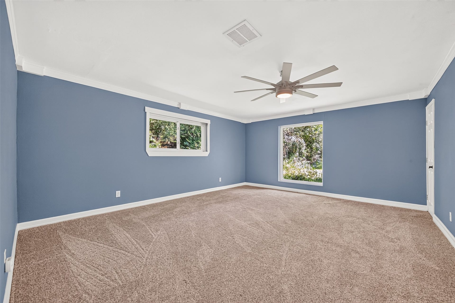 16814 Creeksouth Road, Houston, TX 77068 The spacious primary bedroom features ornate decorative crown molding, a large picture window overlooking the serene backyard, brand-new storm windows, plush carpeting, a modern seven-blade ceiling fan, and soothing new blue paint that creates a calm and inviting retreat.