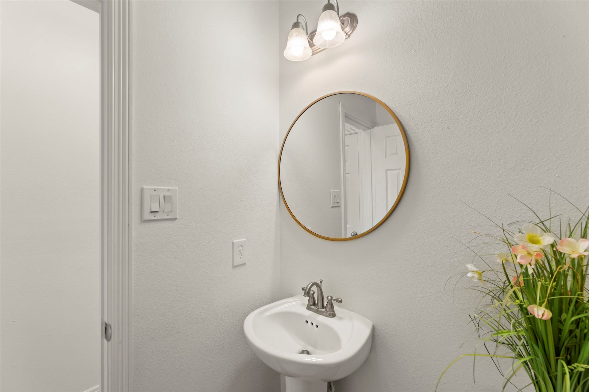 4534 Montcliff Bend Lane, Sugar Land, TX 77479 Lovely powder room with a sleek pedestal sink, round mirror, and elegant lighting, complemented by fresh floral accents for a touch of style.