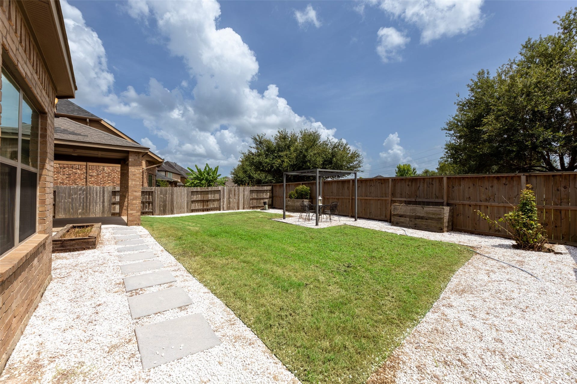 4534 Montcliff Bend Lane, Sugar Land, TX 77479 Well-maintained lawn, stone pathway, and a charming pergola for outdoor relaxation, all enclosed by a wooden fence for privacy.