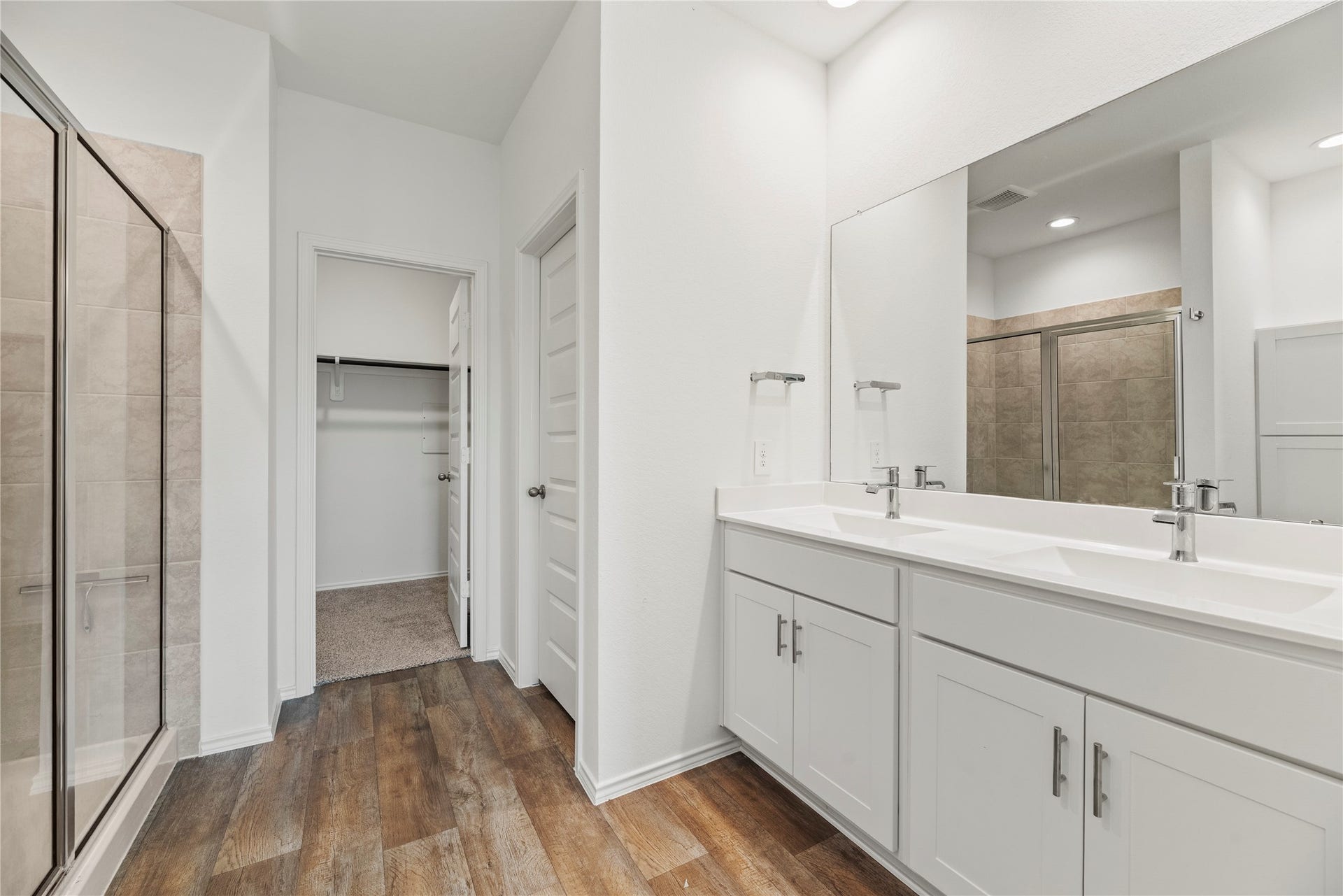 The primary en-suite bathroom offers modern dual vanities, a large mirror, and easy access to the generous walk-in closet.