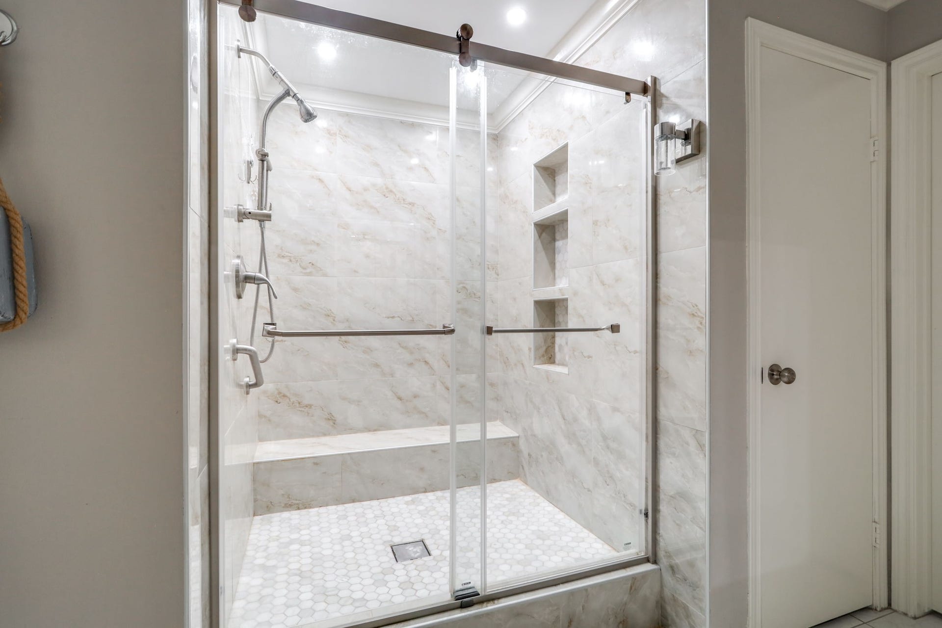 2912 Camelot Lane, Missouri City, TX 77459 The primary bathrooms glass-enclosed shower pairs large-format, marble-look wall tile with a mosaic tile floor. A built-in bench, recessed storage niches, handheld showerhead, and grab bars add thoughtful functionality. Sliding glass doors showcase the tilework and give this shower a polished, contemporary appearance.