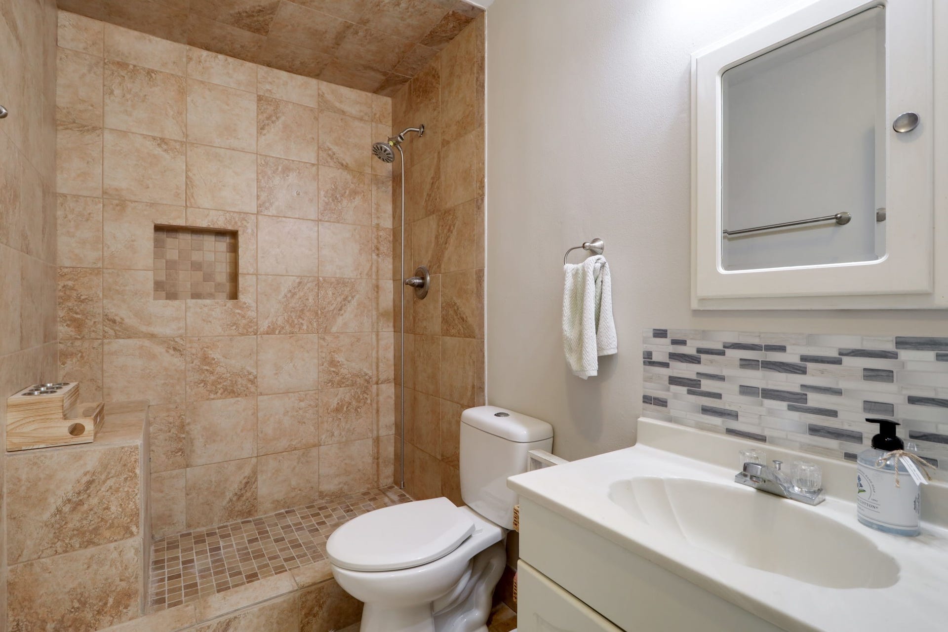 2912 Camelot Lane, Missouri City, TX 77459 The second full bathroom combines a tiled shower with a built-in bench, recessed storage niche, and mosaic shower floor. A single-sink vanity is accented by a decorative backsplash and mirrored medicine cabinet. These details bring texture and practical storage to a bathroom conveniently available beyond the primary suite.