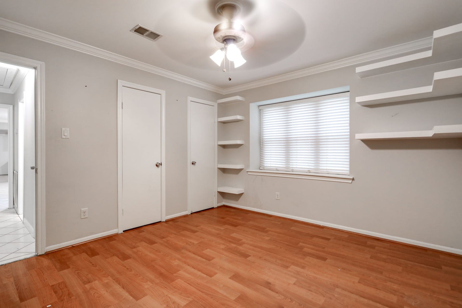 2912 Camelot Lane, Missouri City, TX 77459 This second bedroom view highlights two closet doors and wall-mounted shelving arranged around the window. Wood-look laminate flooring adds warmth, while neutral finishes provide a versatile backdrop for decorating. Storage and display options make the room adaptable for everyday use within this two-bedroom Missouri City townhome.