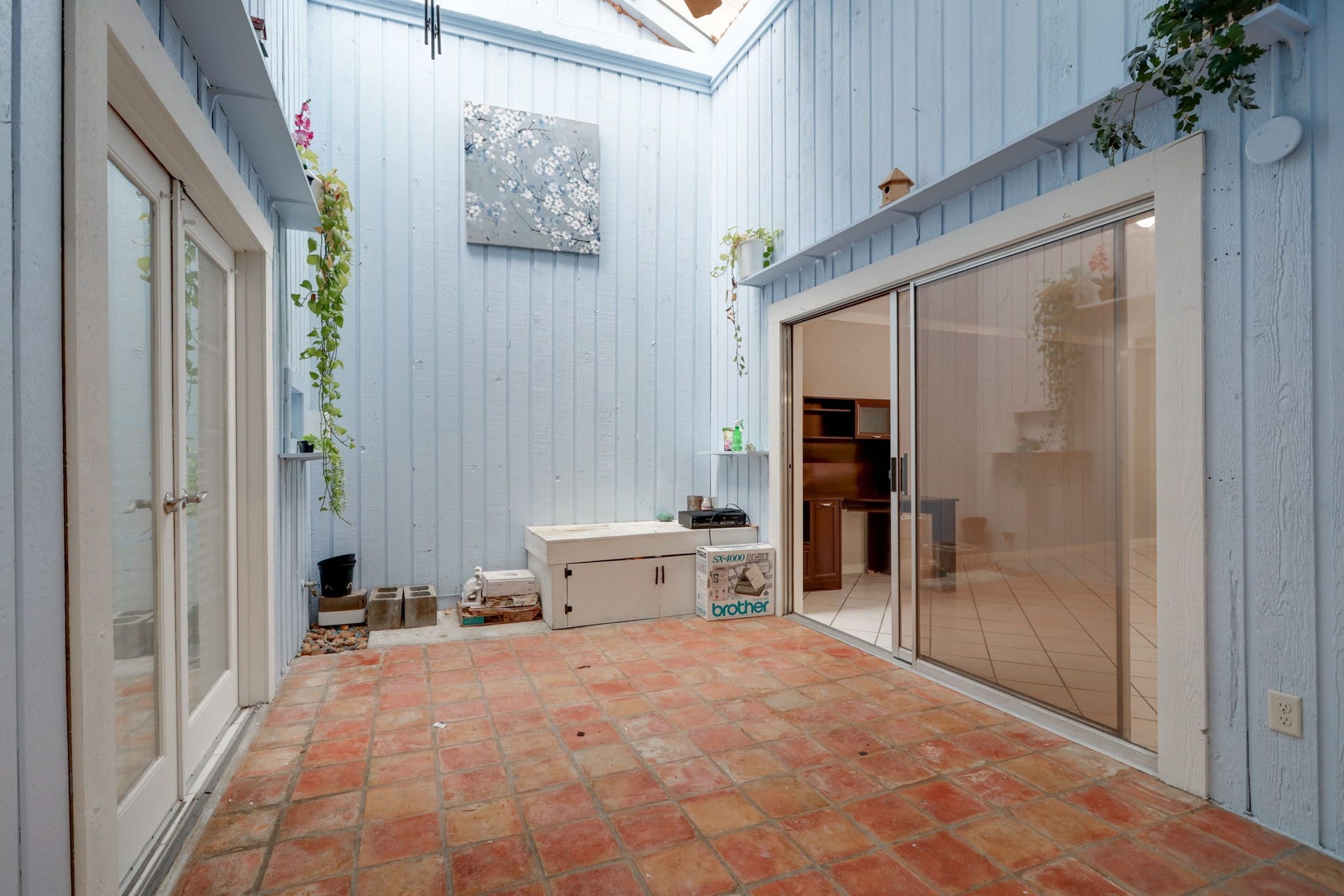 2912 Camelot Lane, Missouri City, TX 77459 Create a favorite reading nook, plant-filled retreat, or intimate sitting area in the central atrium. Terracotta-colored tile flooring contrasts with pale blue siding and white trim, while tall walls draw the eye upward. Glass doors connect adjoining spaces, and French doors link the atrium to the primary bedroom.