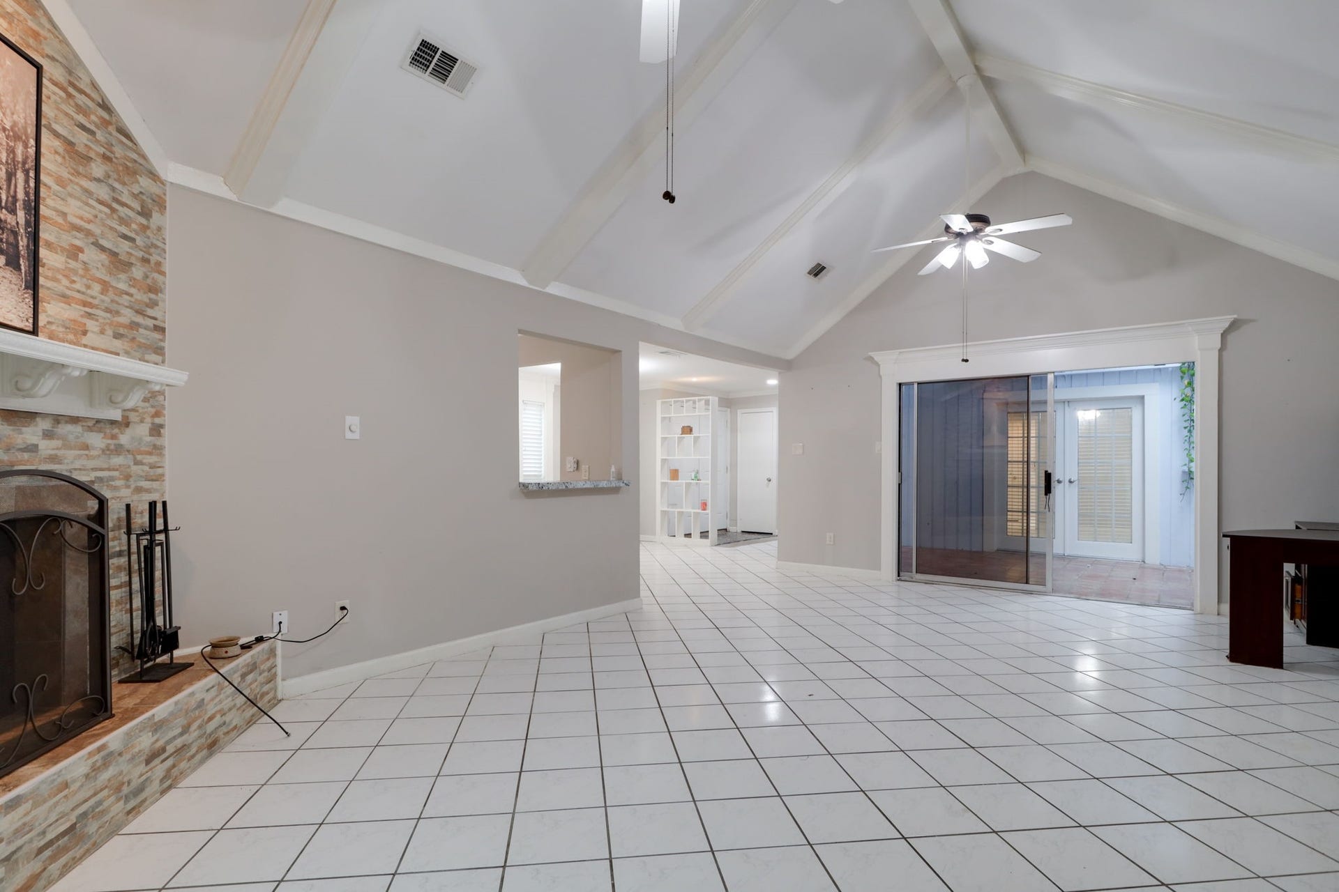 2912 Camelot Lane, Missouri City, TX 77459 This alternate perspective showcases the living rooms generous proportions and connection to the central atrium. Exposed ceiling beams, crown molding, and ceiling fans add detail overhead, while tile flooring extends across the room. Sliding glass doors frame the atrium, giving the main living space another source of natural light and a distinctive view.