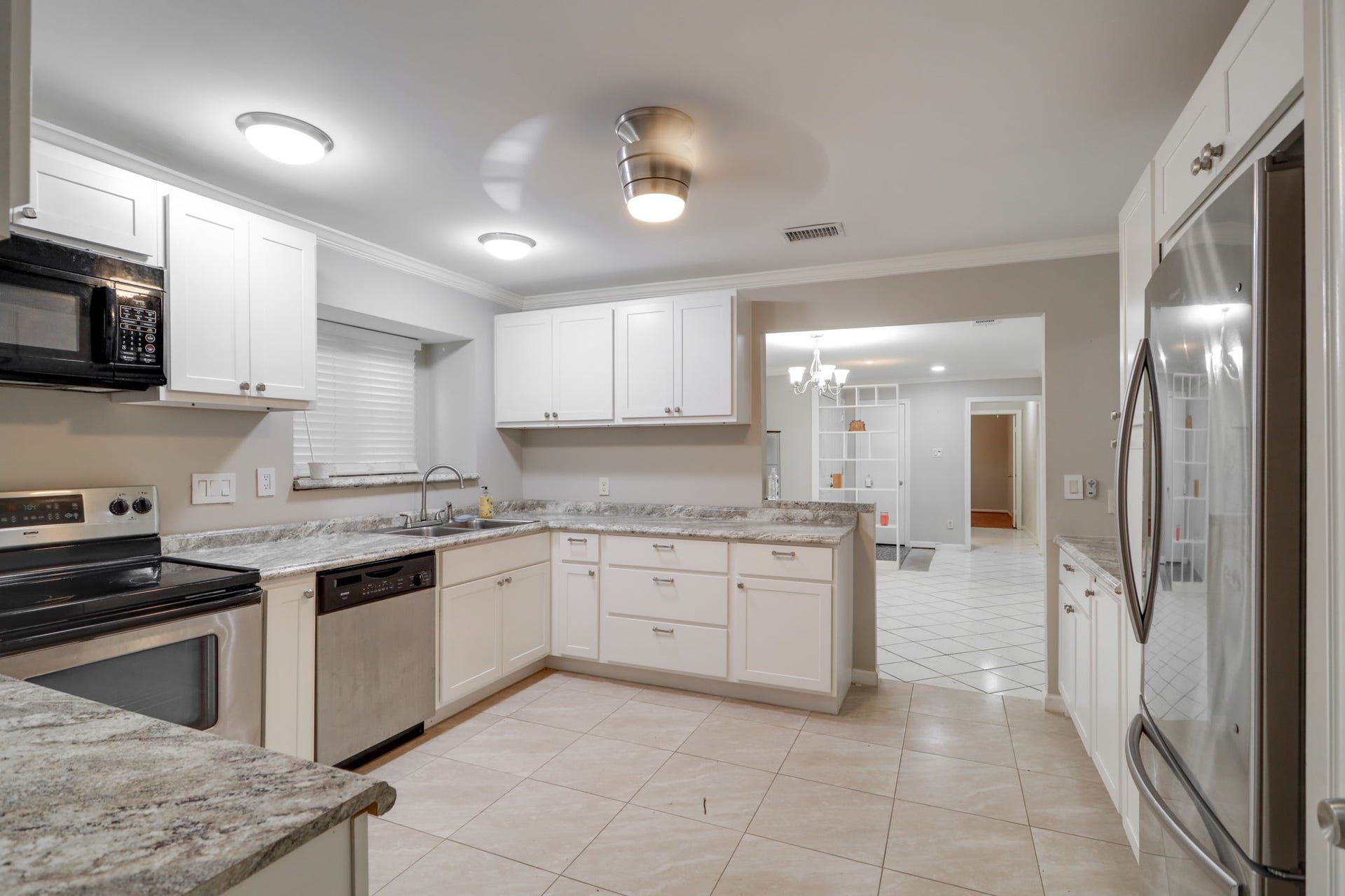 2912 Camelot Lane, Missouri City, TX 77459 Enjoy a kitchen layout that connects meal preparation with dining and entertaining. White cabinetry, a stainless steel dishwasher, and ample counters provide practical workspace, while the wide opening leads directly into the dining room. Tile flooring continues between the rooms, and the kitchens open sightlines help the adjoining spaces feel connected.