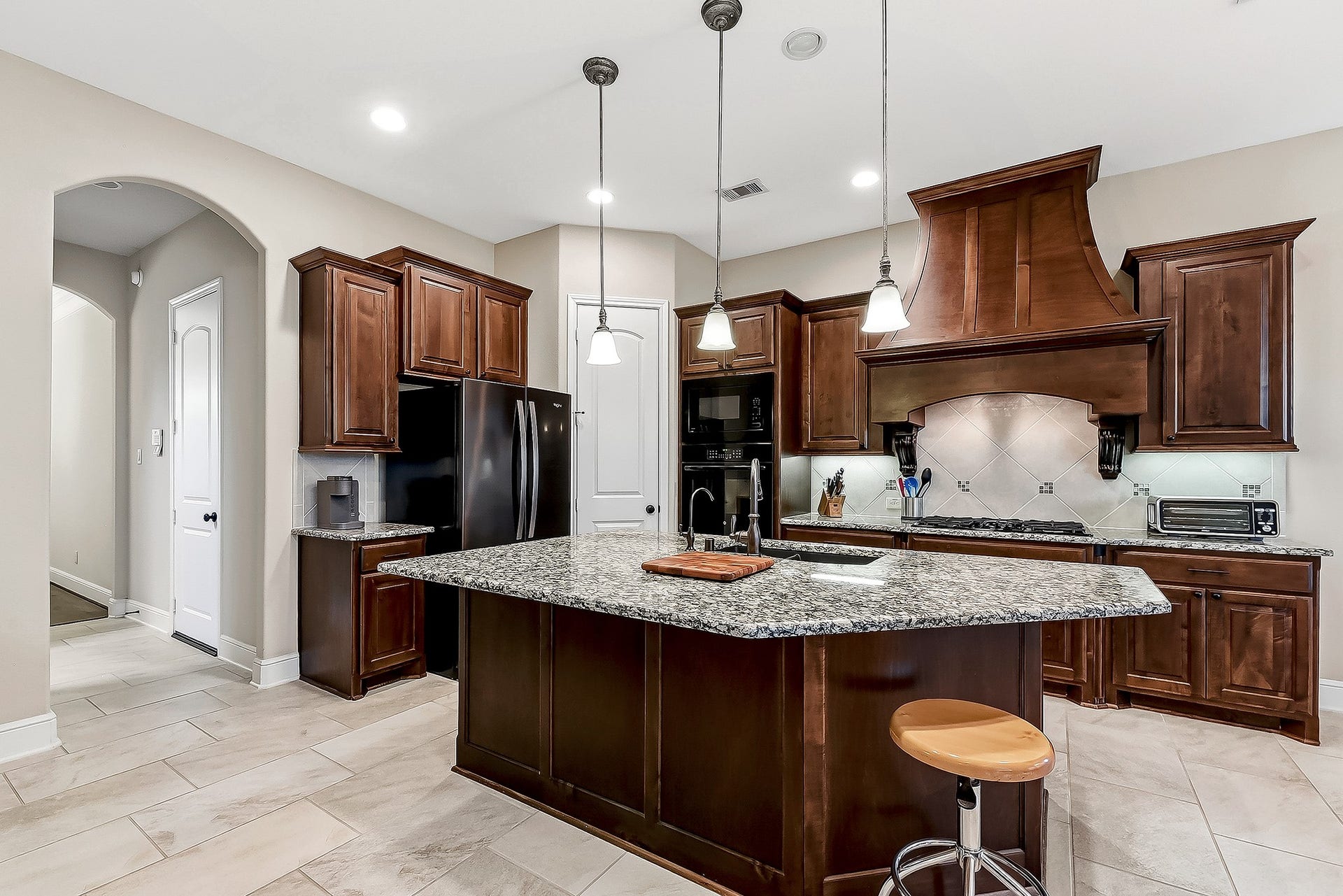 27411 Gladway Manor Drive, Katy, TX 77494 The well-designed kitchen features a spacious breakfast bar with seating, granite countertops, a tiled backsplash, gas cooktop, and built-in wall oven and microwave. A large walk-in pantry provides abundant storage, while pendant lighting adds a stylish finishing touch over the breakfast bar. To the right is the inviting breakfast room, while to the left, leads toward the formal dining room or back to the three-car garage, creating an easy and functional flow throughout the home.